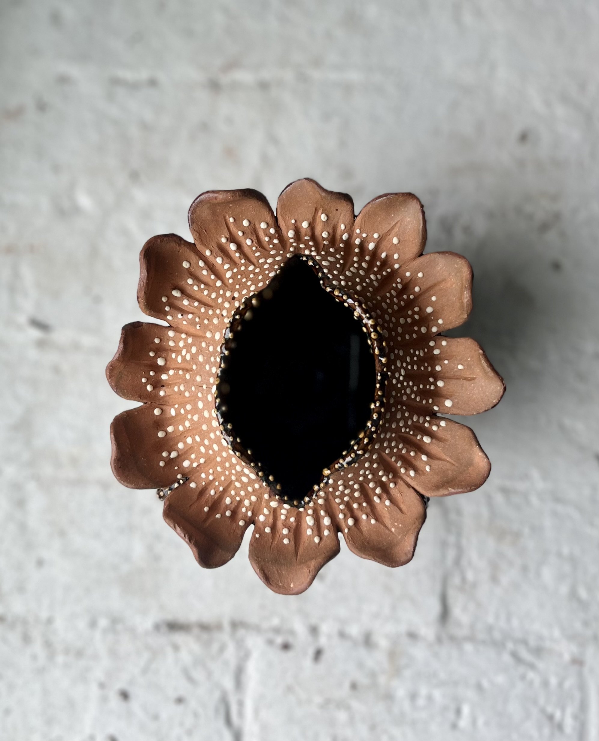 Decorative flower-shaped container with a black center and white dotted patterns on the petal edges, set against a white brick wall background.