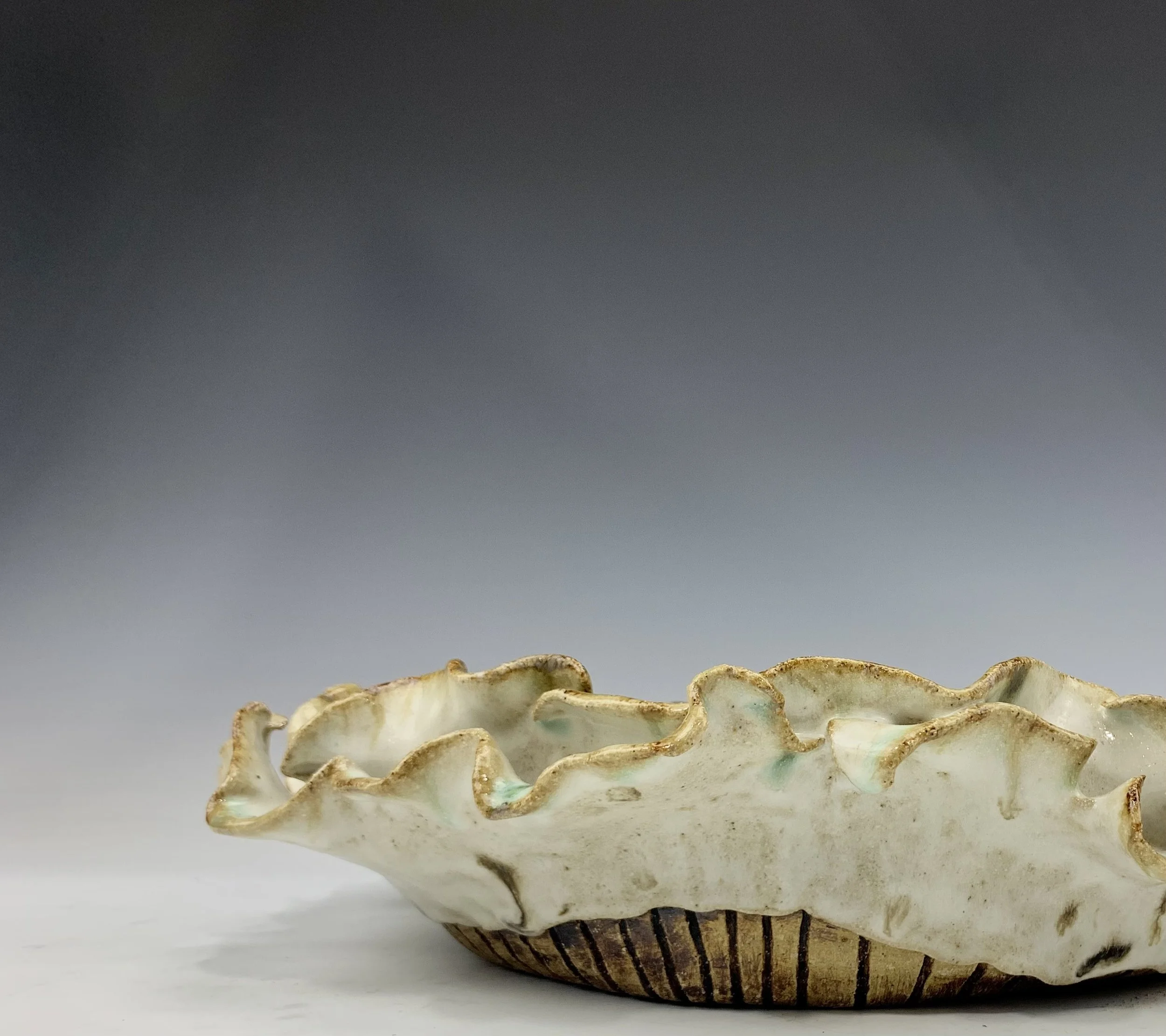A ceramic bowl with an irregular, ruffled edge and a glazed finish, sitting on a white surface against a gradient background.