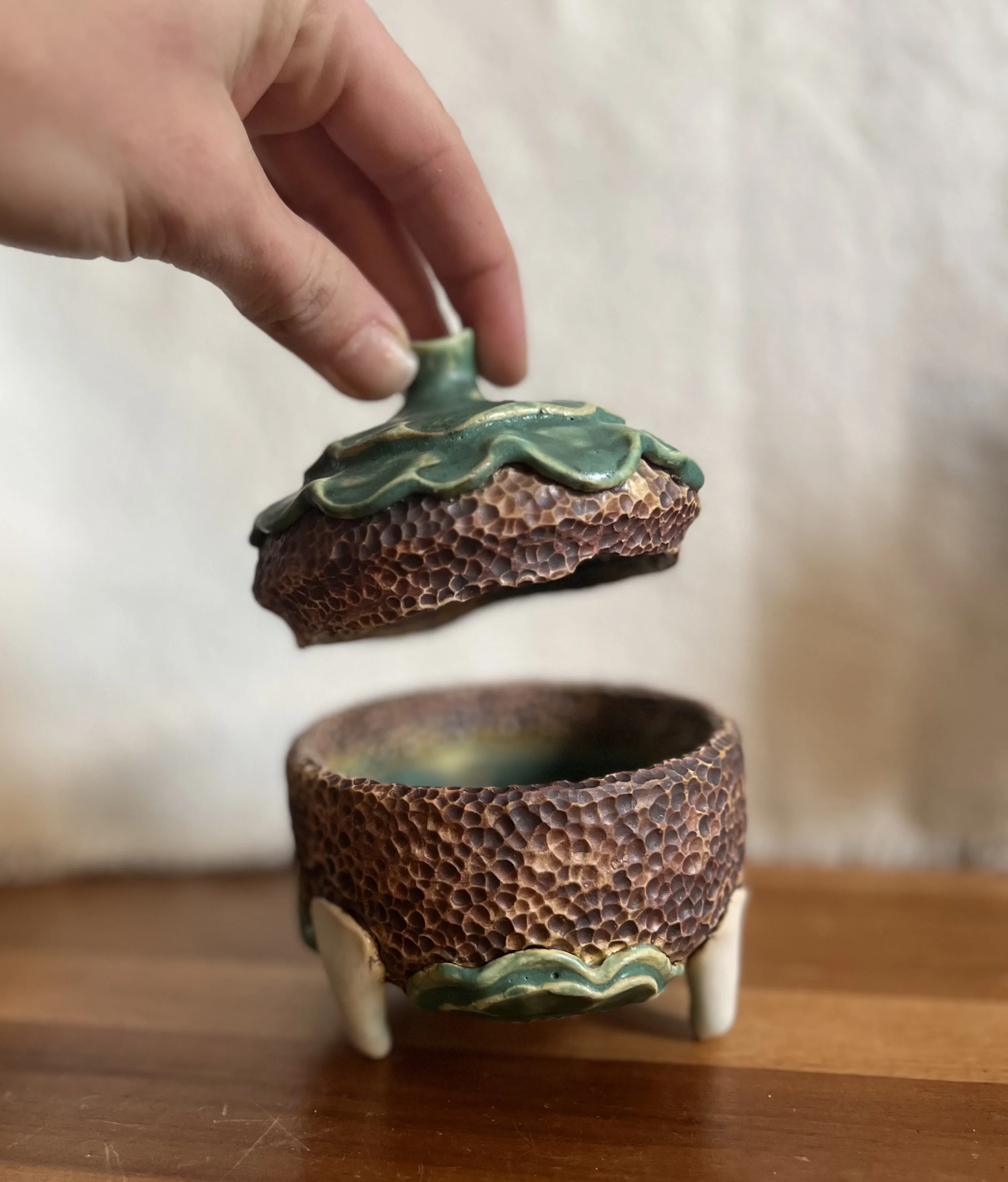 A ceramic container shaped like a strawberry, with a removable top, resting on a wooden surface.