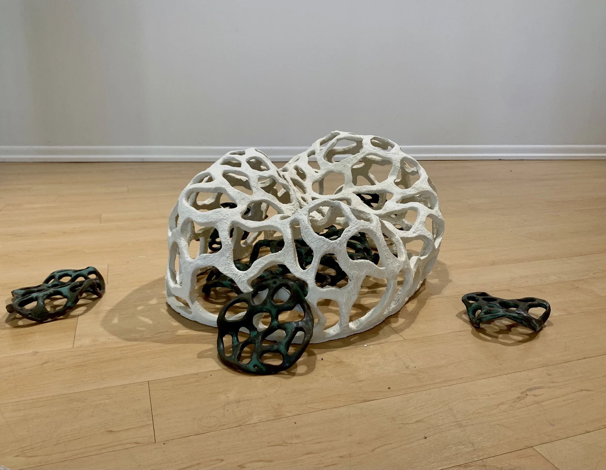 Decorative white and dark green ceramic sculptures with open, organic shapes on a wooden floor against a plain white wall.