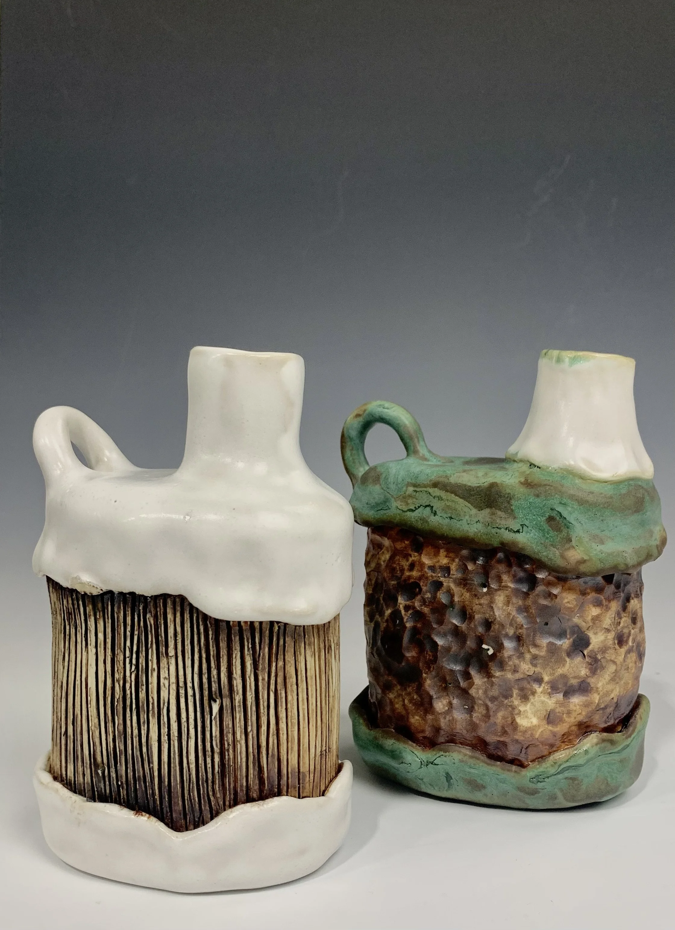 Two ceramic mugs with artistic glaze and textures, one with a wood-like pattern and the other with a rustic, textured surface, displayed against a neutral background.