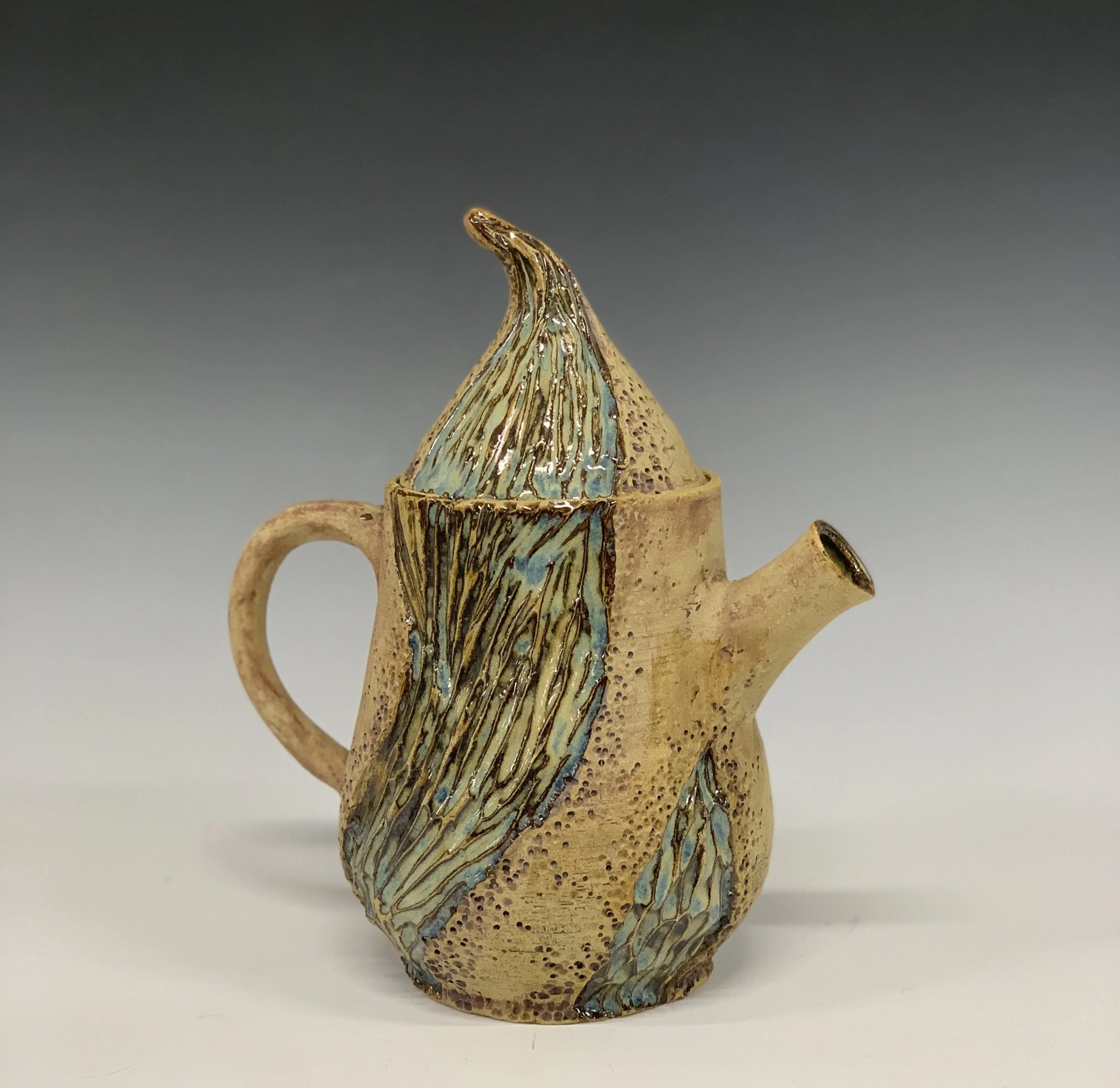 Ceramic teapot designed to resemble a banana with textured surface and blue-green glazed accents.