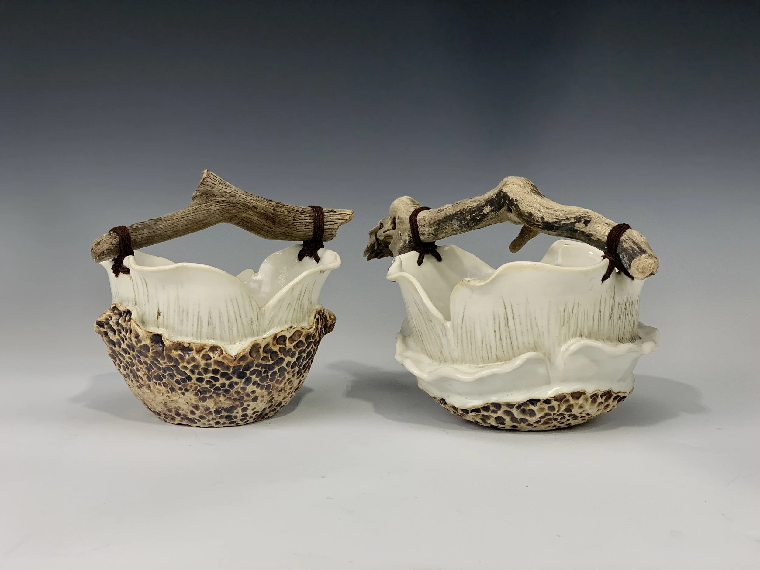 Two ceramic bowls with textured, rough exterior and smooth interior, each with a driftwood handle tied with dark string.