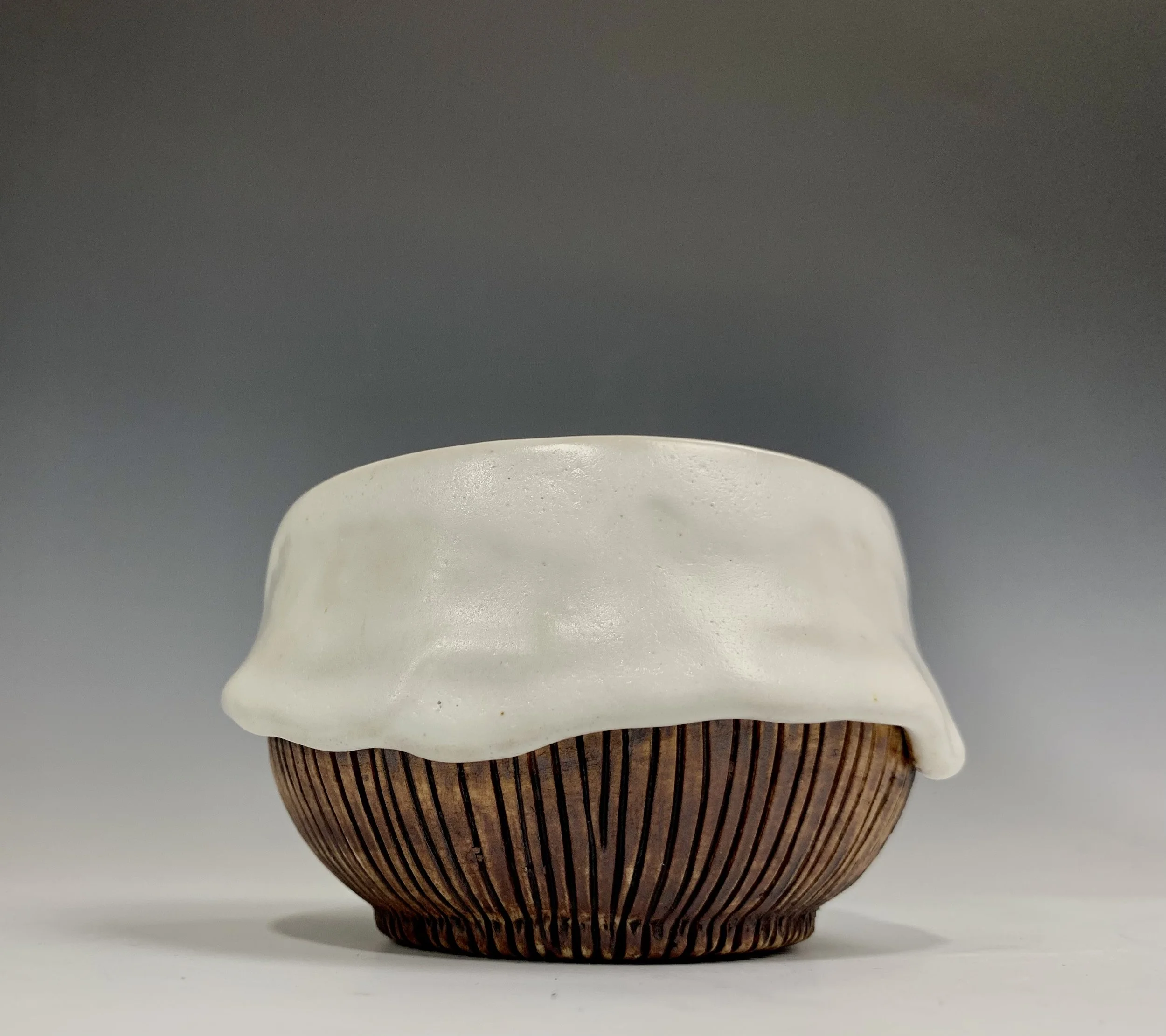 Bowl with a wooden vertical striped pattern, topped with a white, creamy, uneven glaze that drapes over the edges.