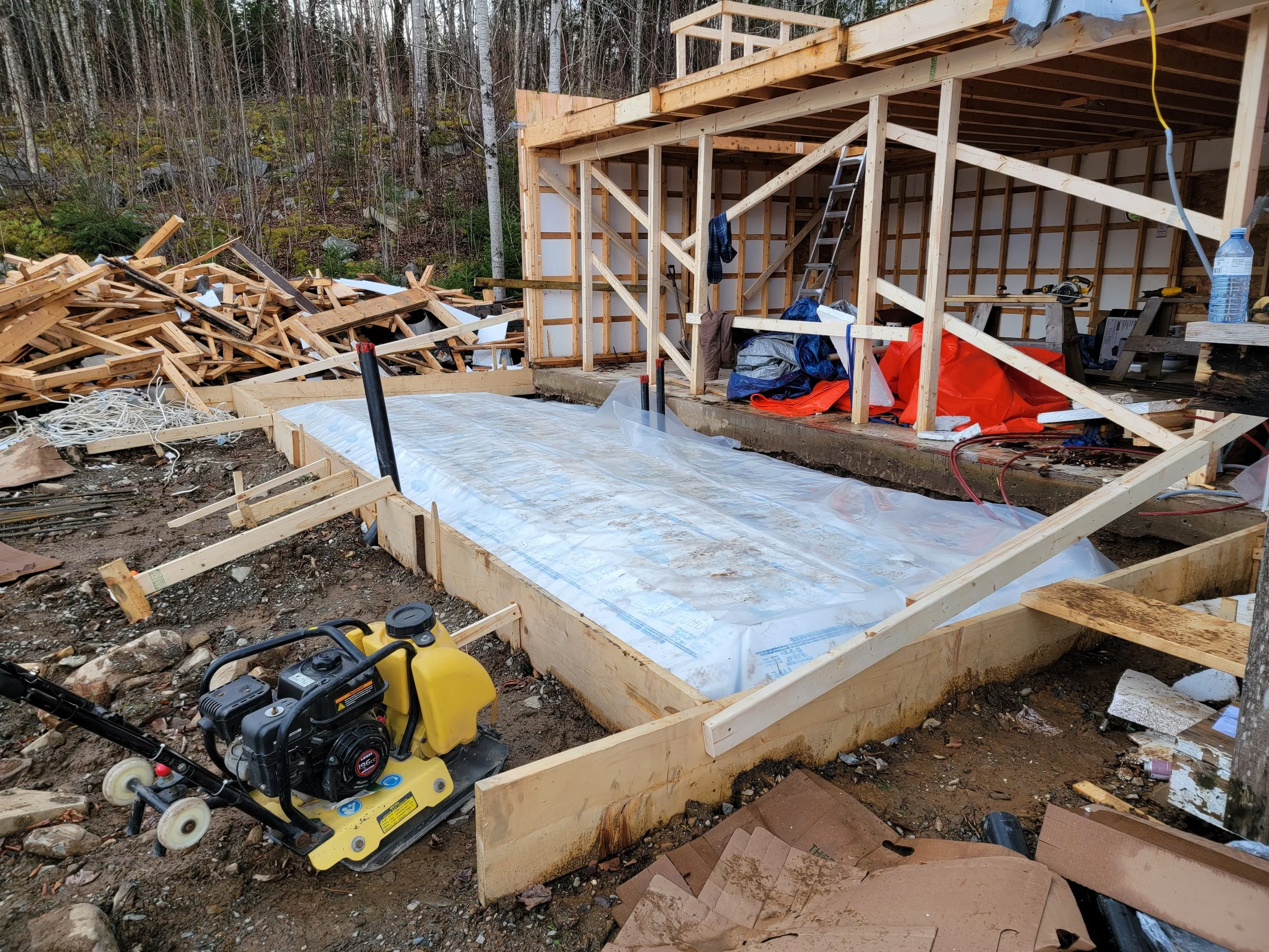 Construction site with wooden framework, a plastic sheet on the ground, construction tools, and debris, indicating ongoing building work for a house or structure.