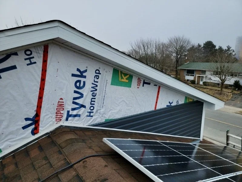 Close-up of a house roof with solar panels and new roofing underlayment visible on the sloped side.
