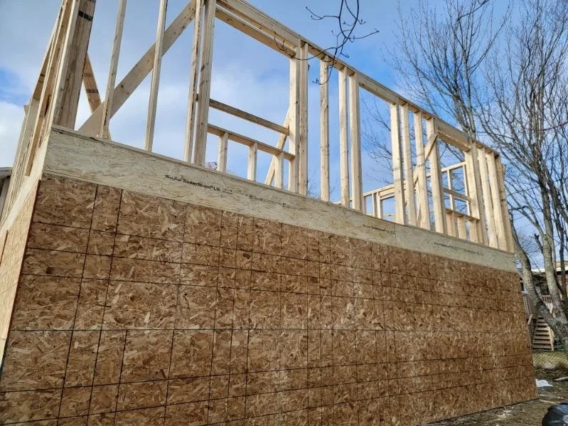 Wooden framing for a building under construction, with OSB sheathing on the lower half, and framing for windows and walls above.