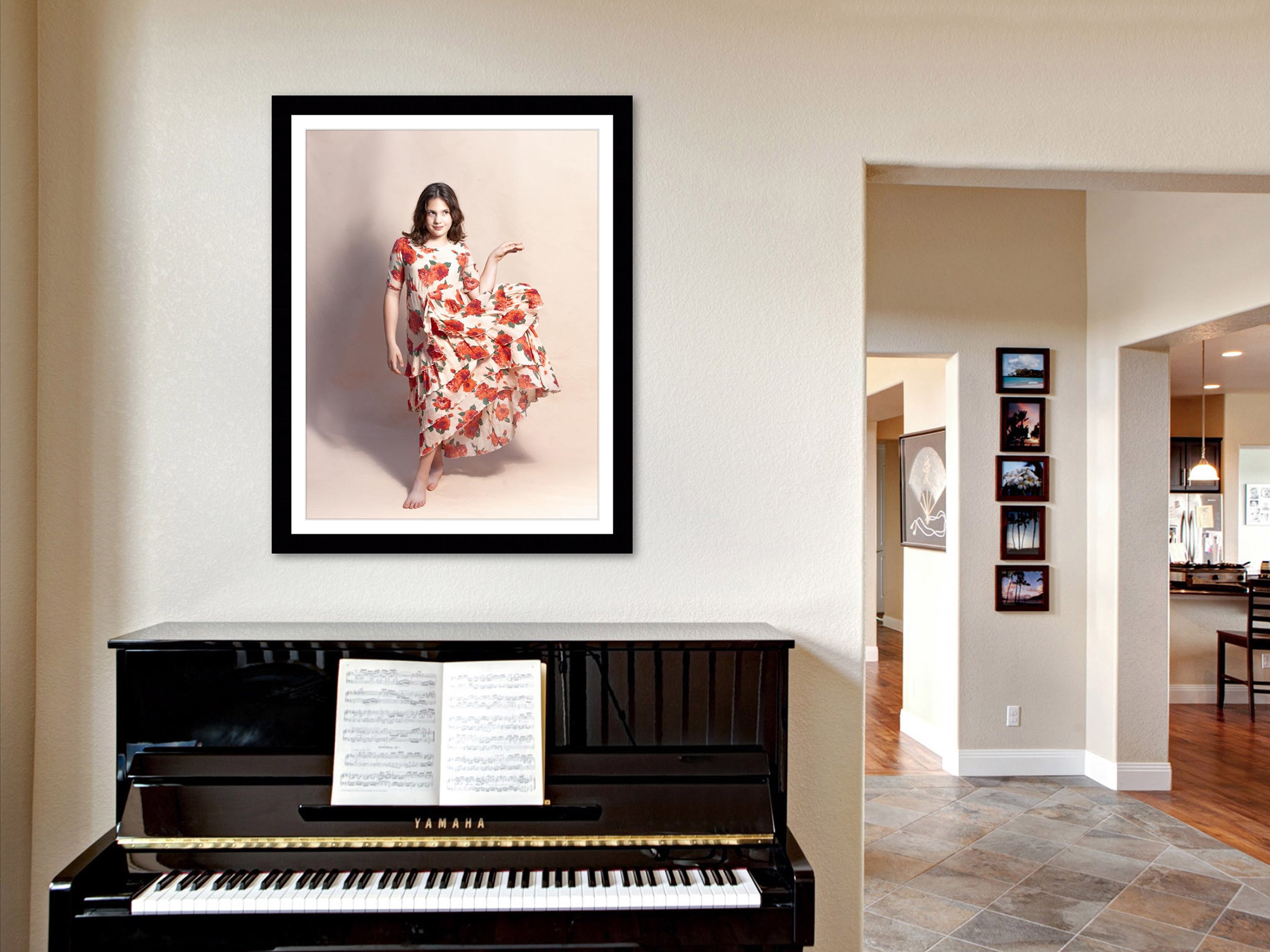 A black Yamaha piano with sheet music on the stand, situated in a modern living room. Above the piano is a framed portrait of a woman in a floral dress. The room features tiled flooring and a view of an open kitchen area with visible artwork and phot