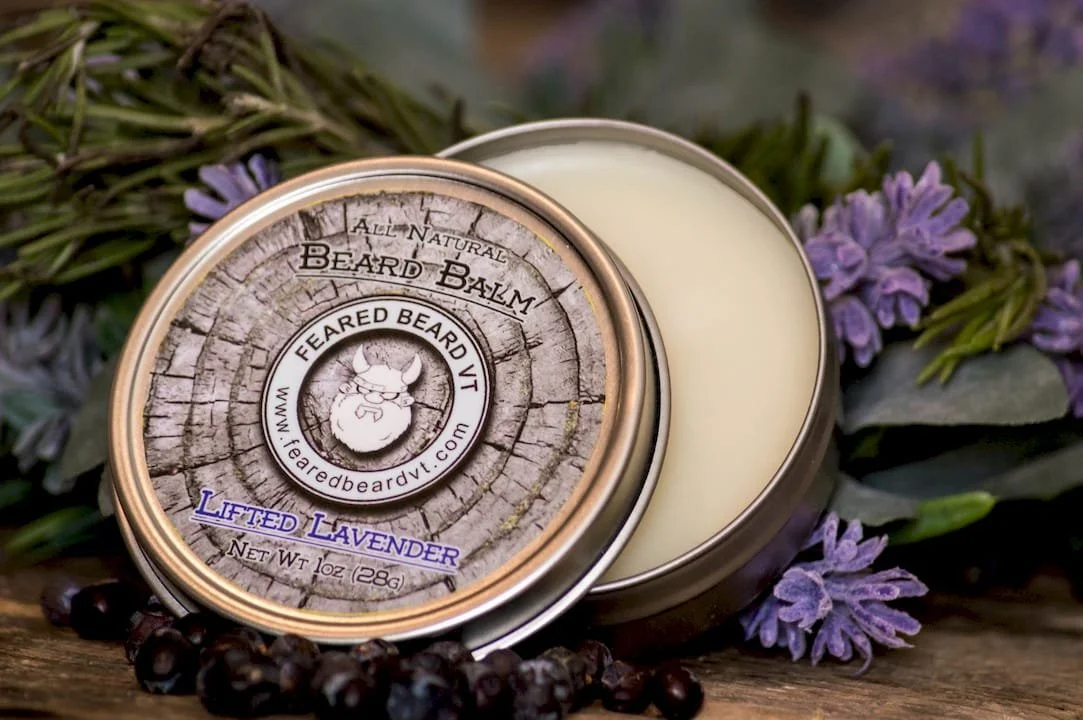 A tin container of Feared Beard Balm labeled "Lifted Lavender" surrounded by lavender flowers