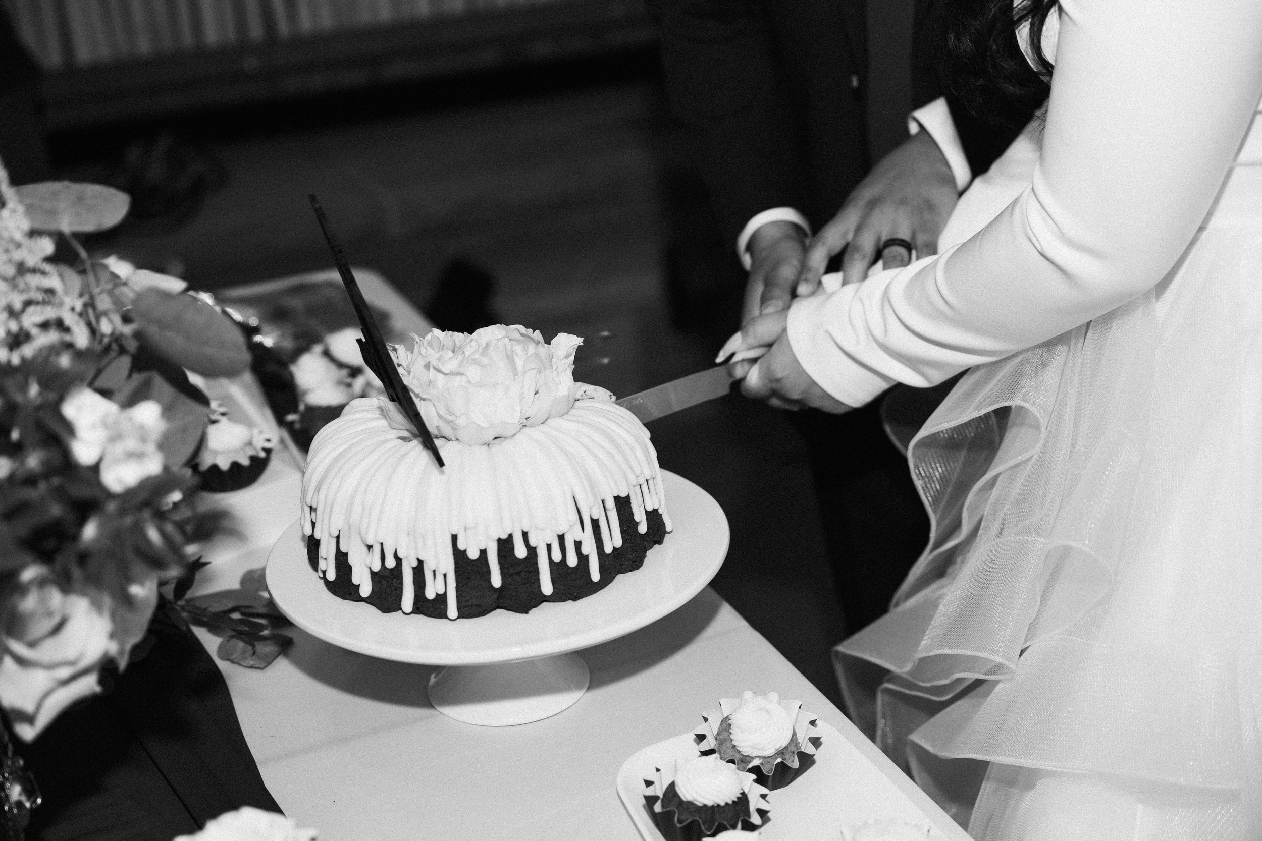 A couple in wedding attire cutting a wedding cake together at a celebration.