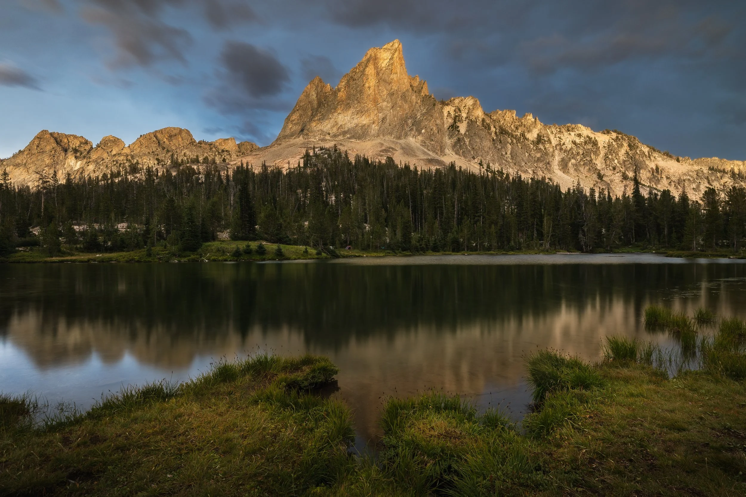 A mountain with a lake and forest in front during a cloudy evening.