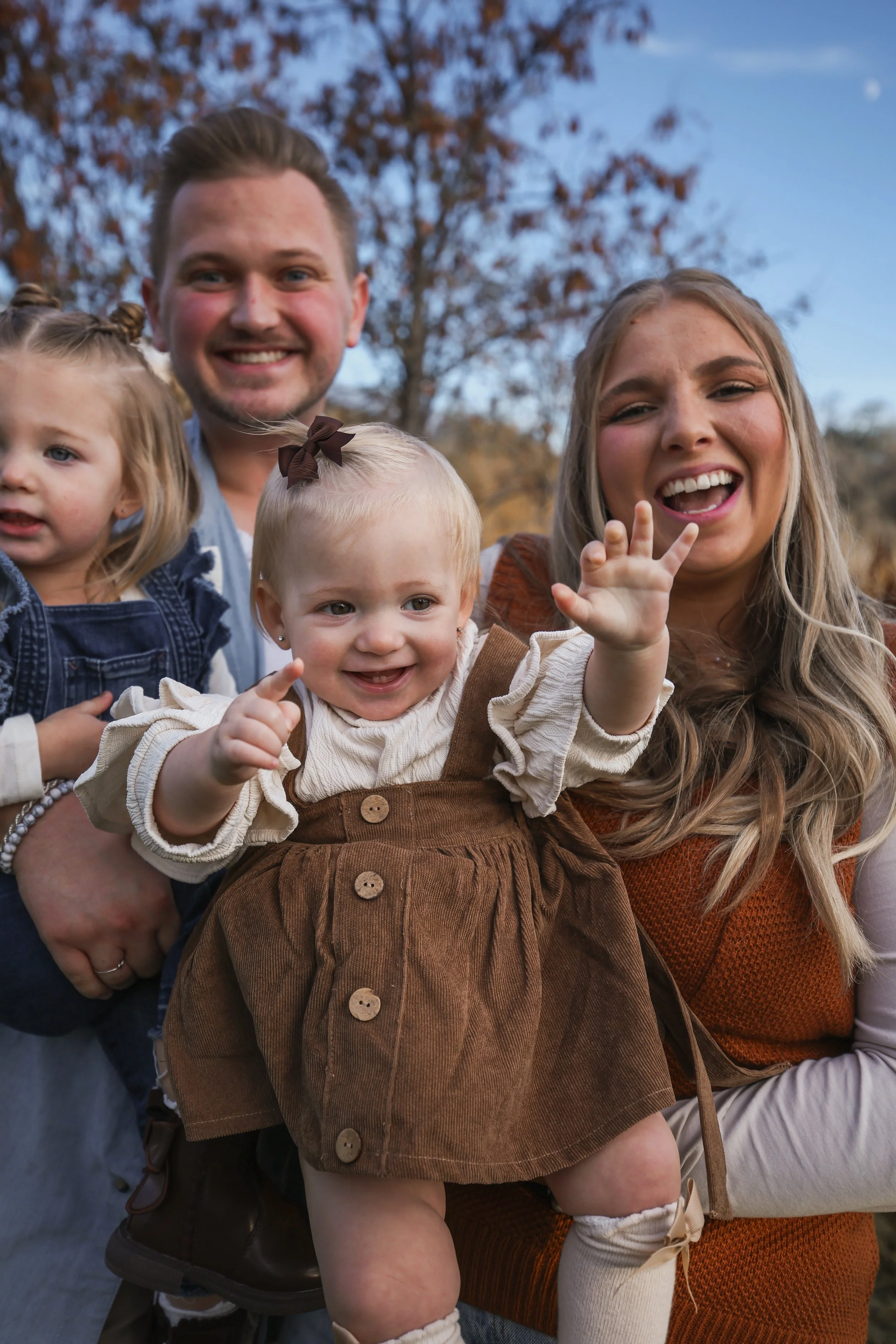 A family of four outdoors, smiling and laughing, with autumn trees in the background.