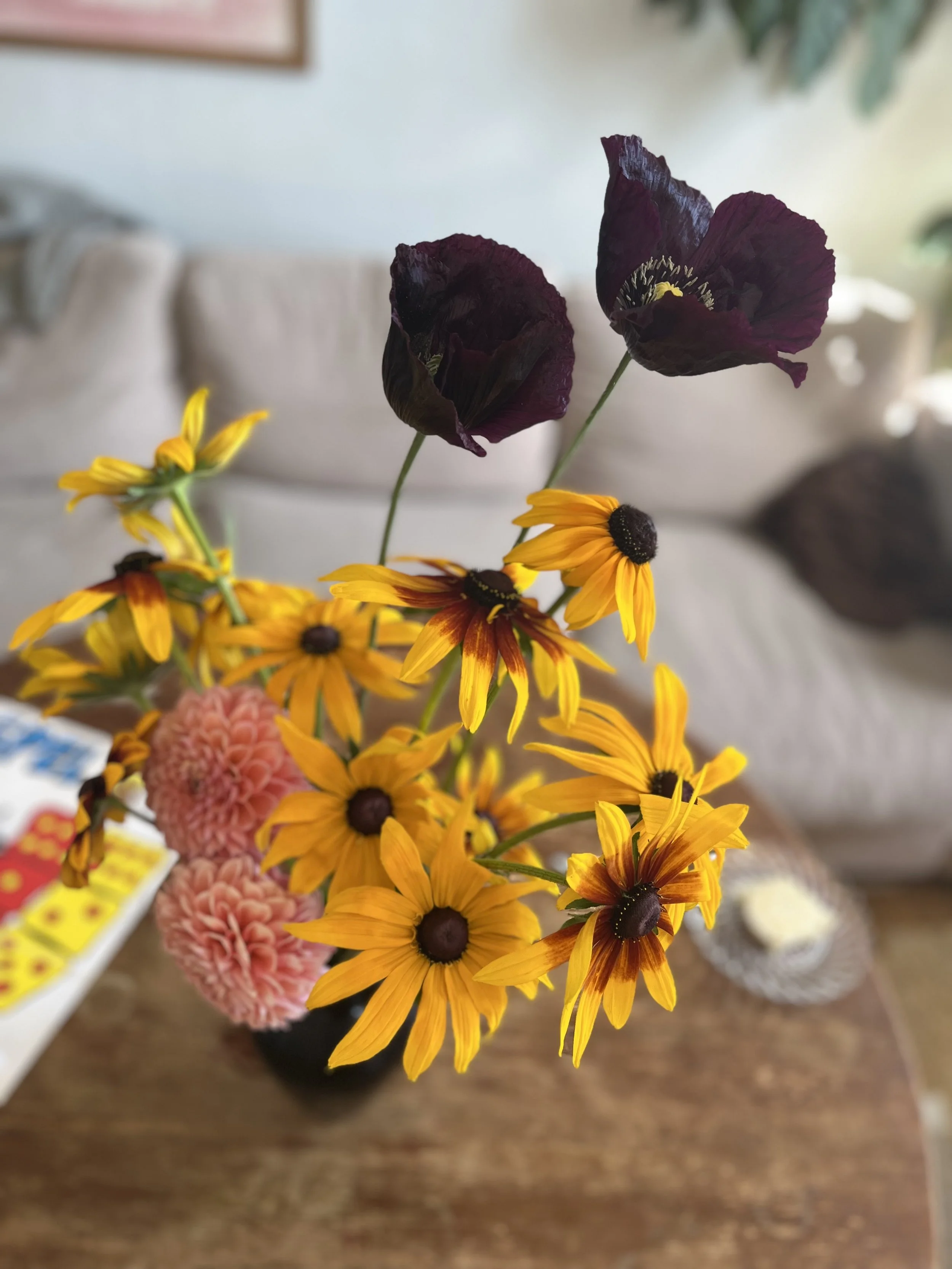 Blommor i en vas på ett träbord, inklusive svart vallmo och rudbeckia.