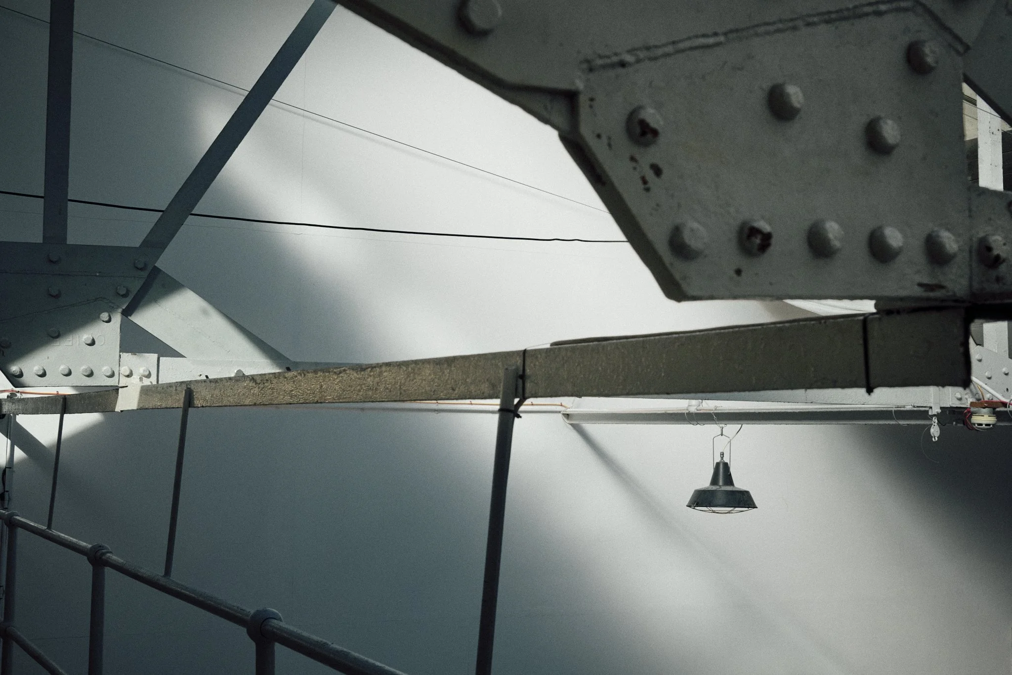 Close-up of metal structure and railing with an industrial-style hanging light in the background under a cloudy sky.