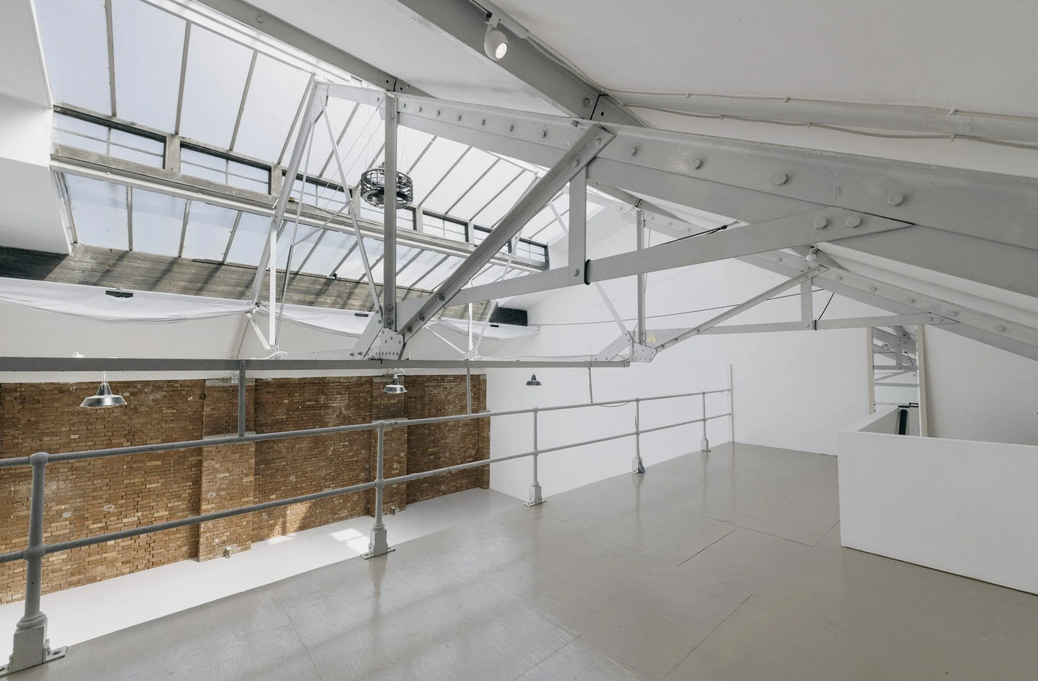 Interior of a modern industrial-style building with exposed brick wall, white metal beams, and large skylight windows letting in natural light.