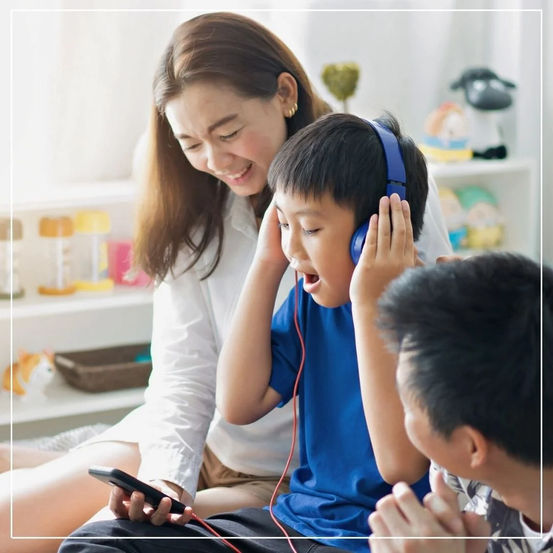 Asian mother, child, and father practicing mindful breathing with the My Friend Breath resources using a phone and headphones.