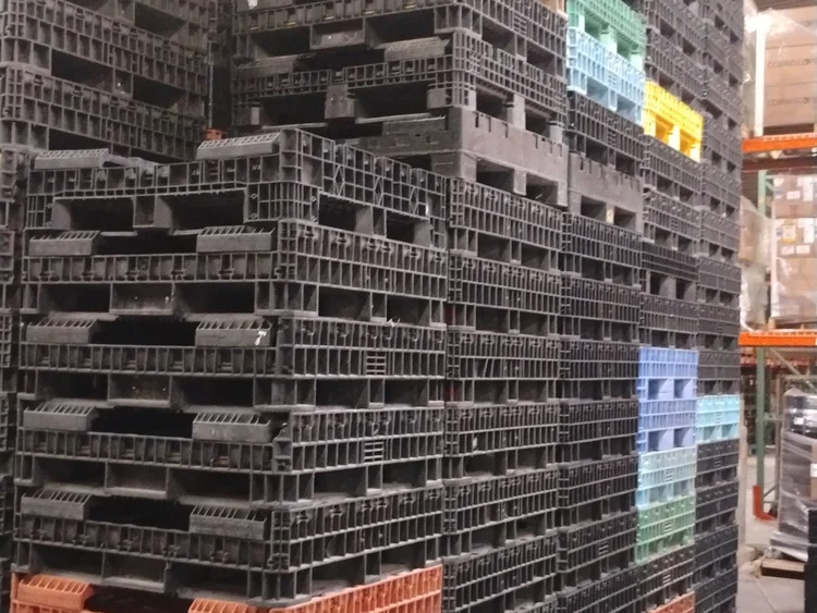 Pilas de contenedores plásticos negros y de colores en un almacén