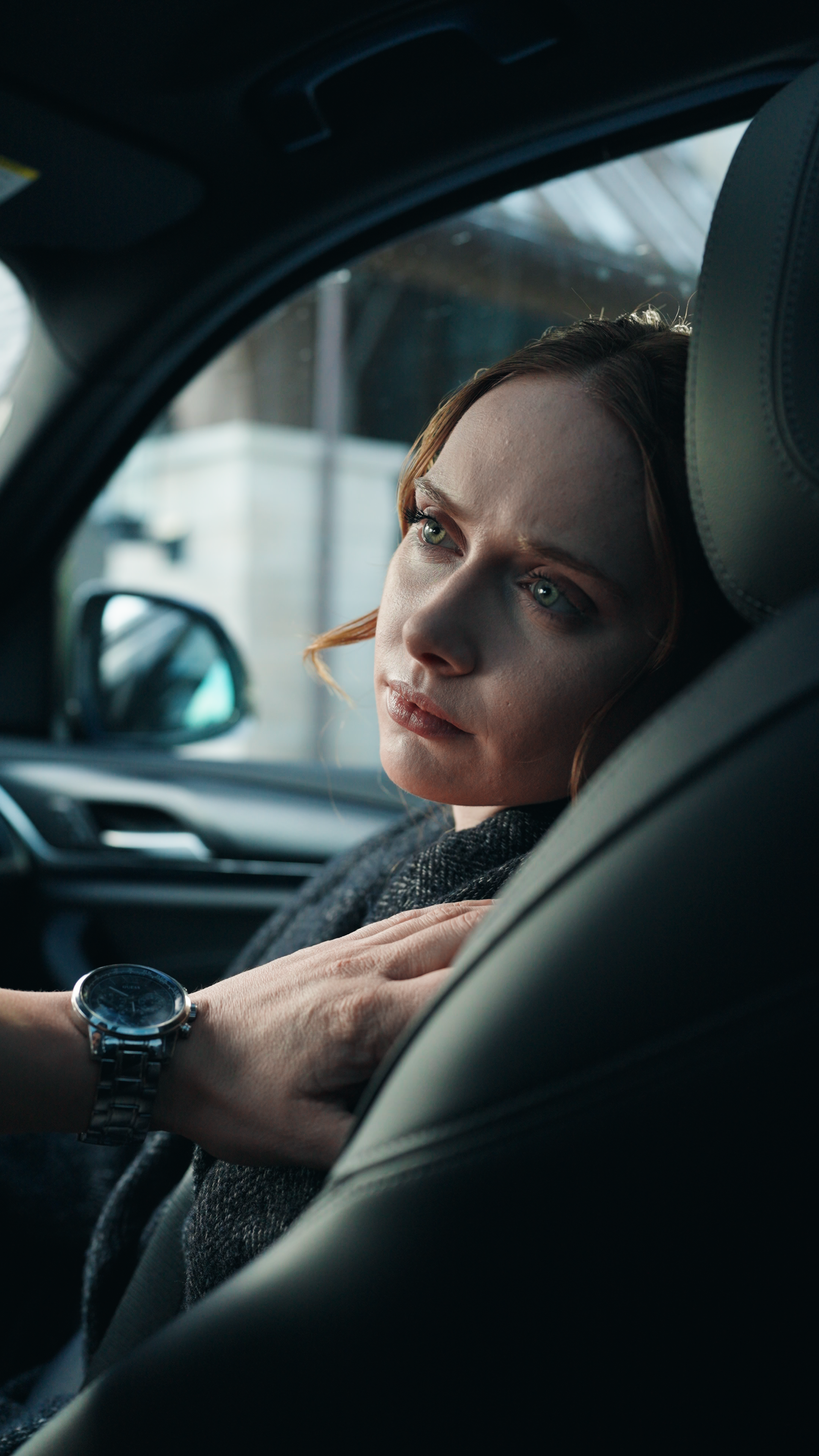 Woman seated in the passenger seat of a car looking toward the driver while a man’s hand rests on her shoulder.