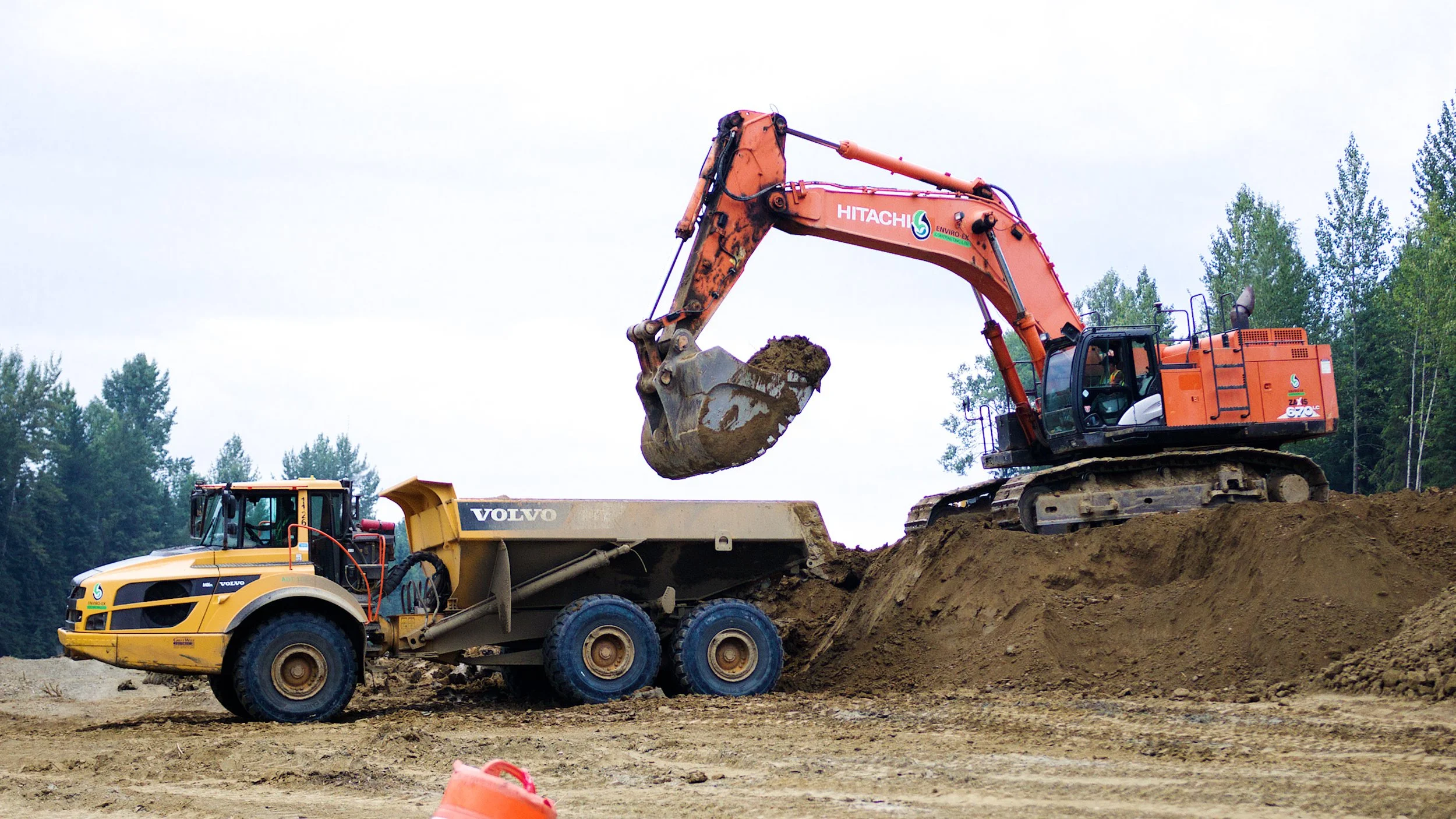Excavator loading soil into a dump truck at a construction site.