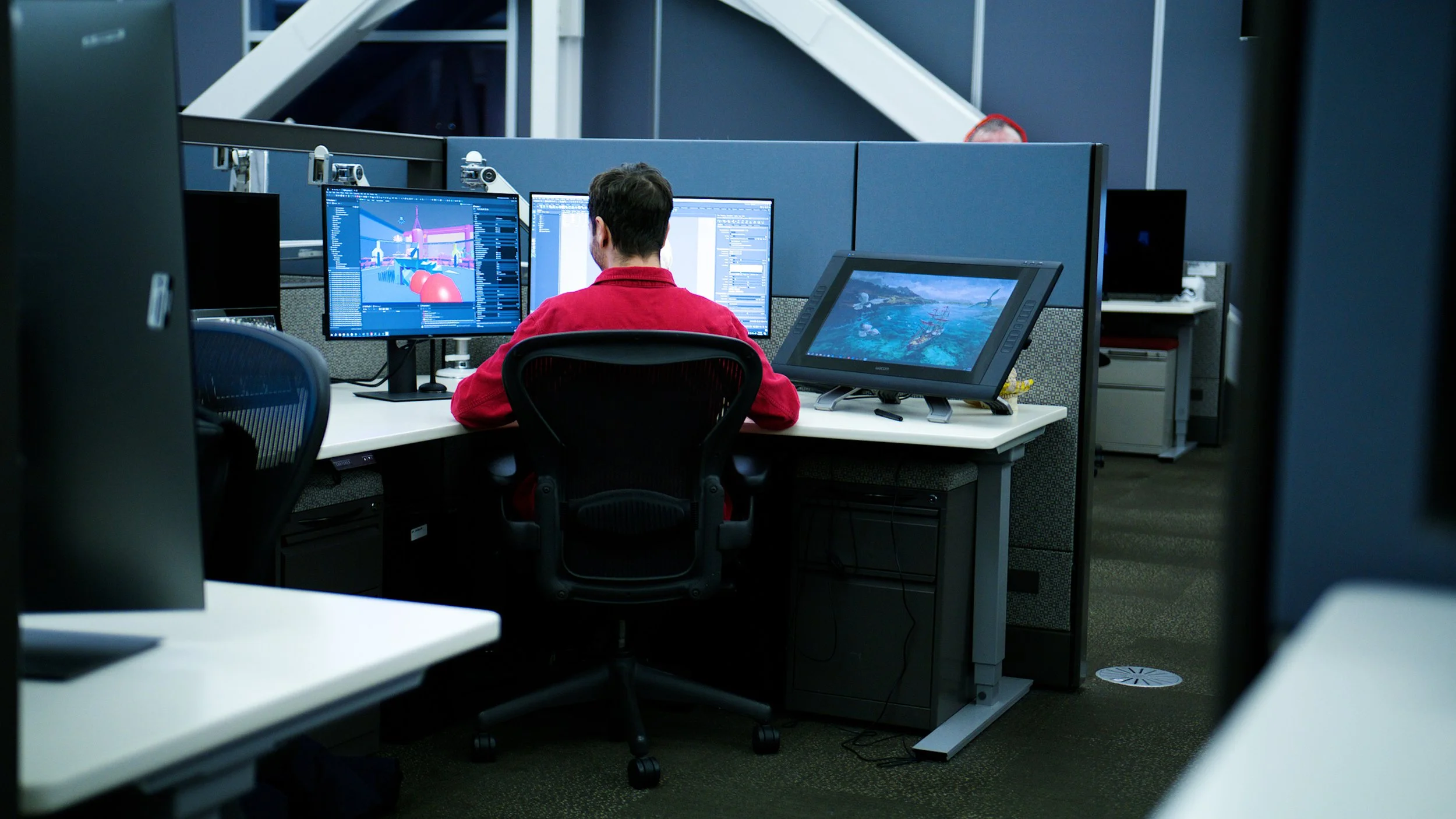 Game developer working at a computer with multiple monitors displaying 3D game environments.