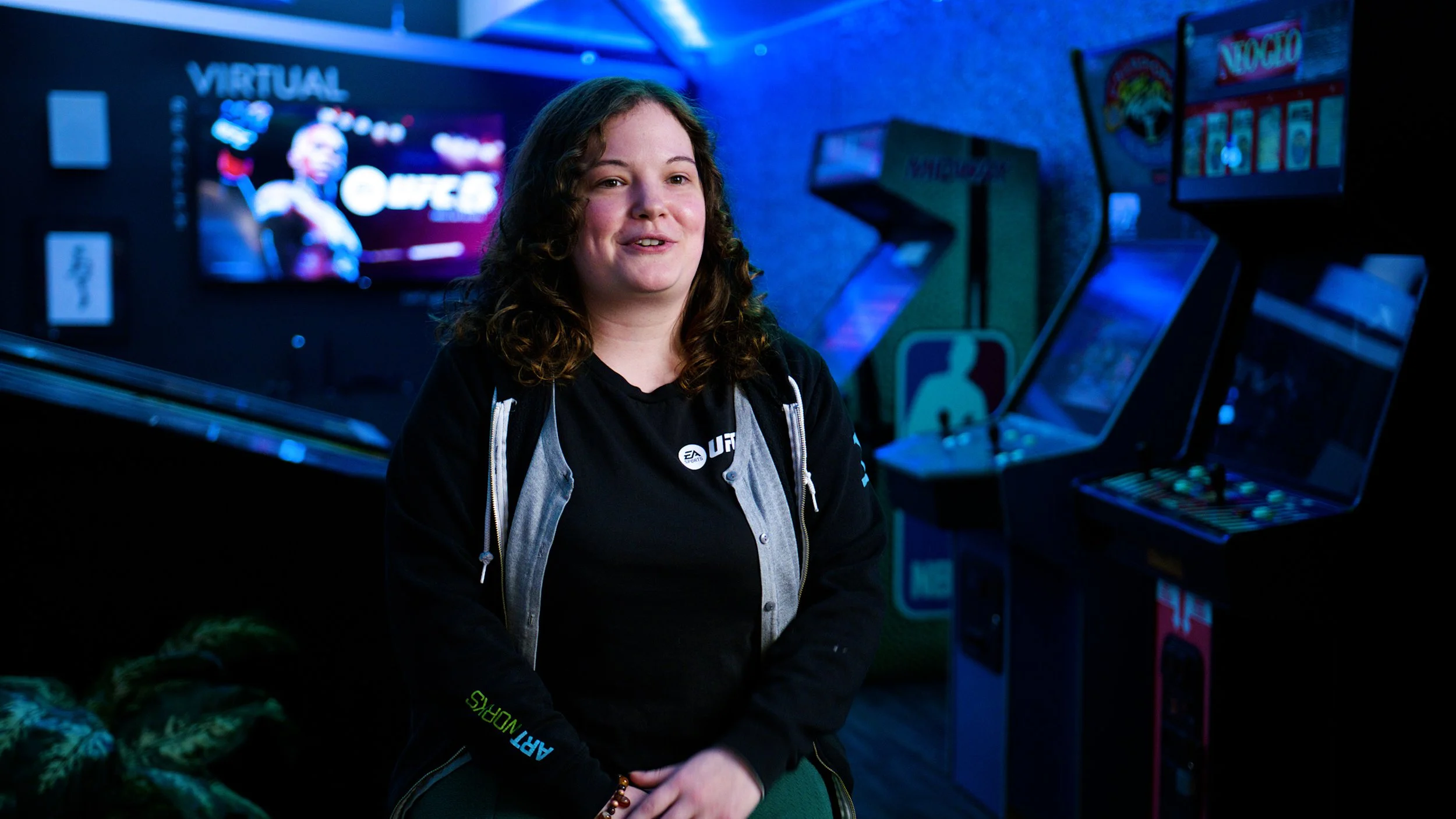 EA Sports team member interviewed in a studio environment with arcade machines in the background.