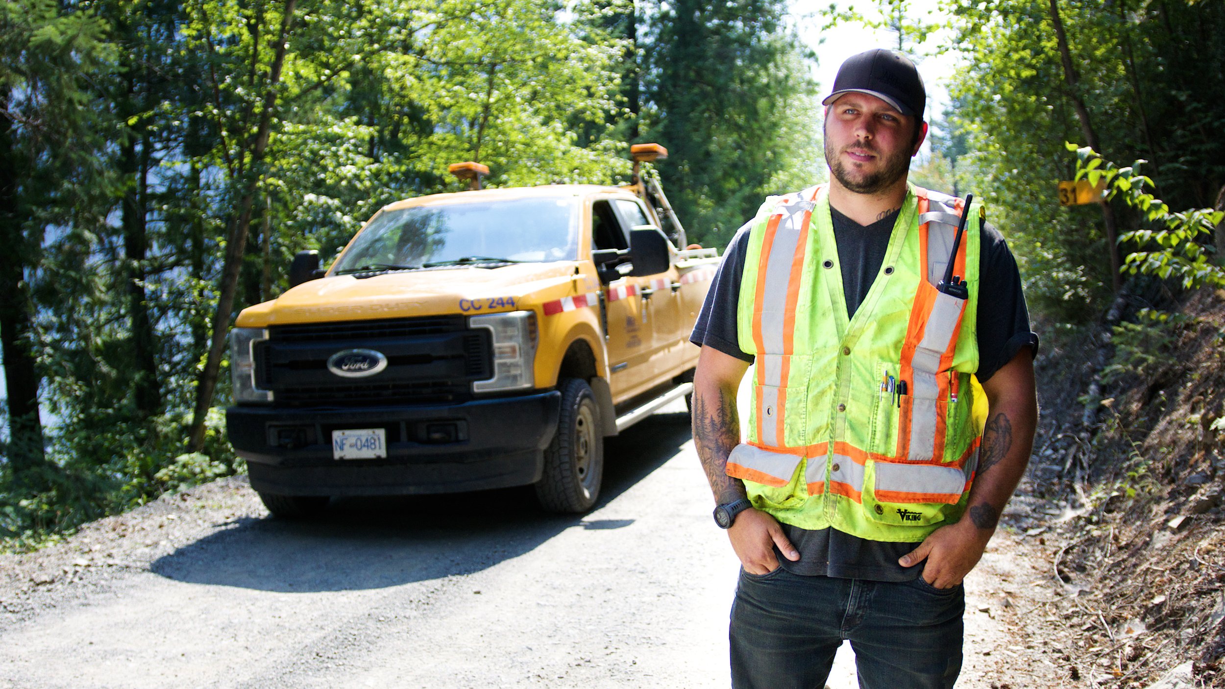 Road construction worker standing beside a service truck on a forest roadway.