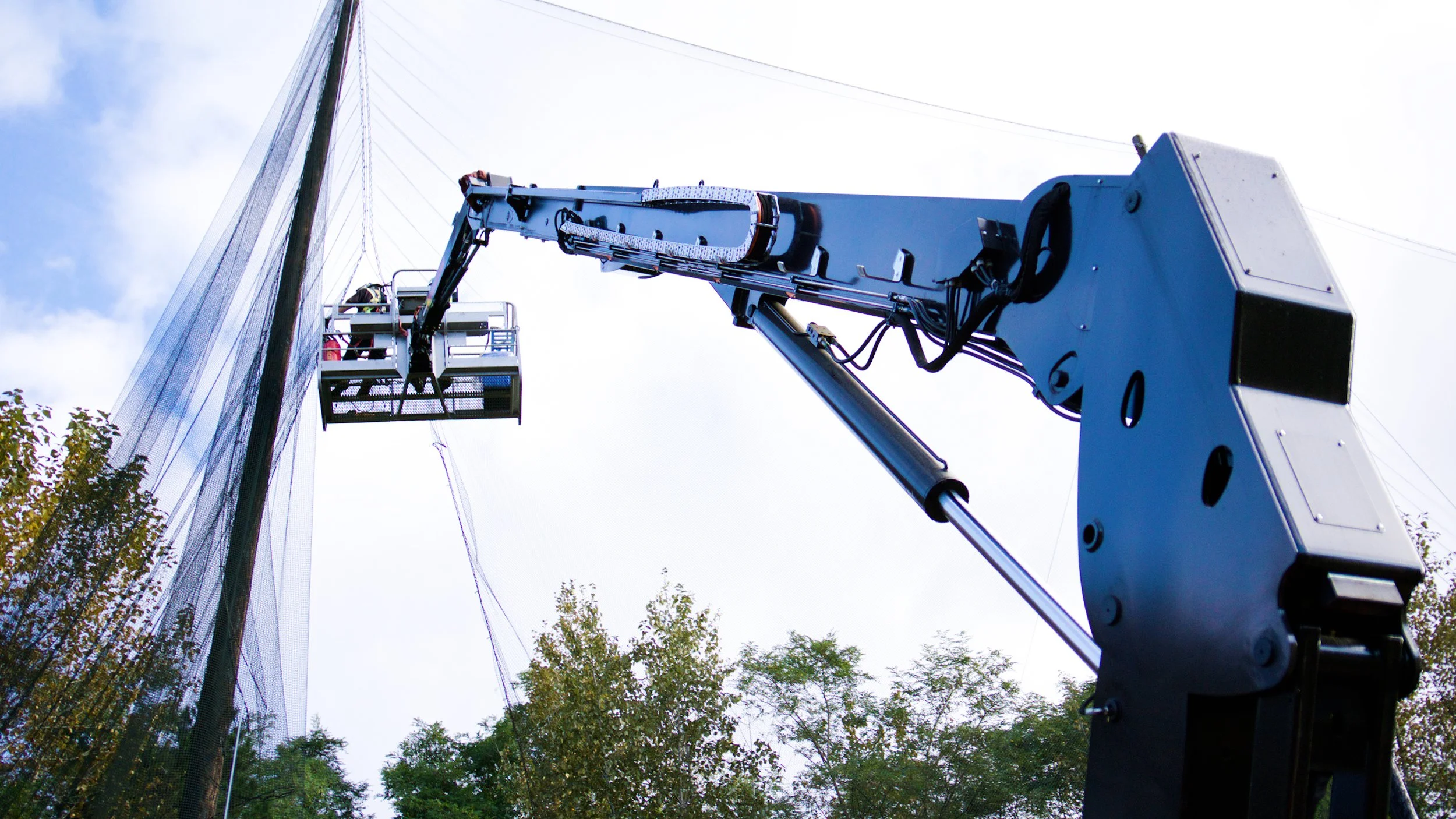 Construction worker operating a boom lift to remove safety netting at a demolition site.