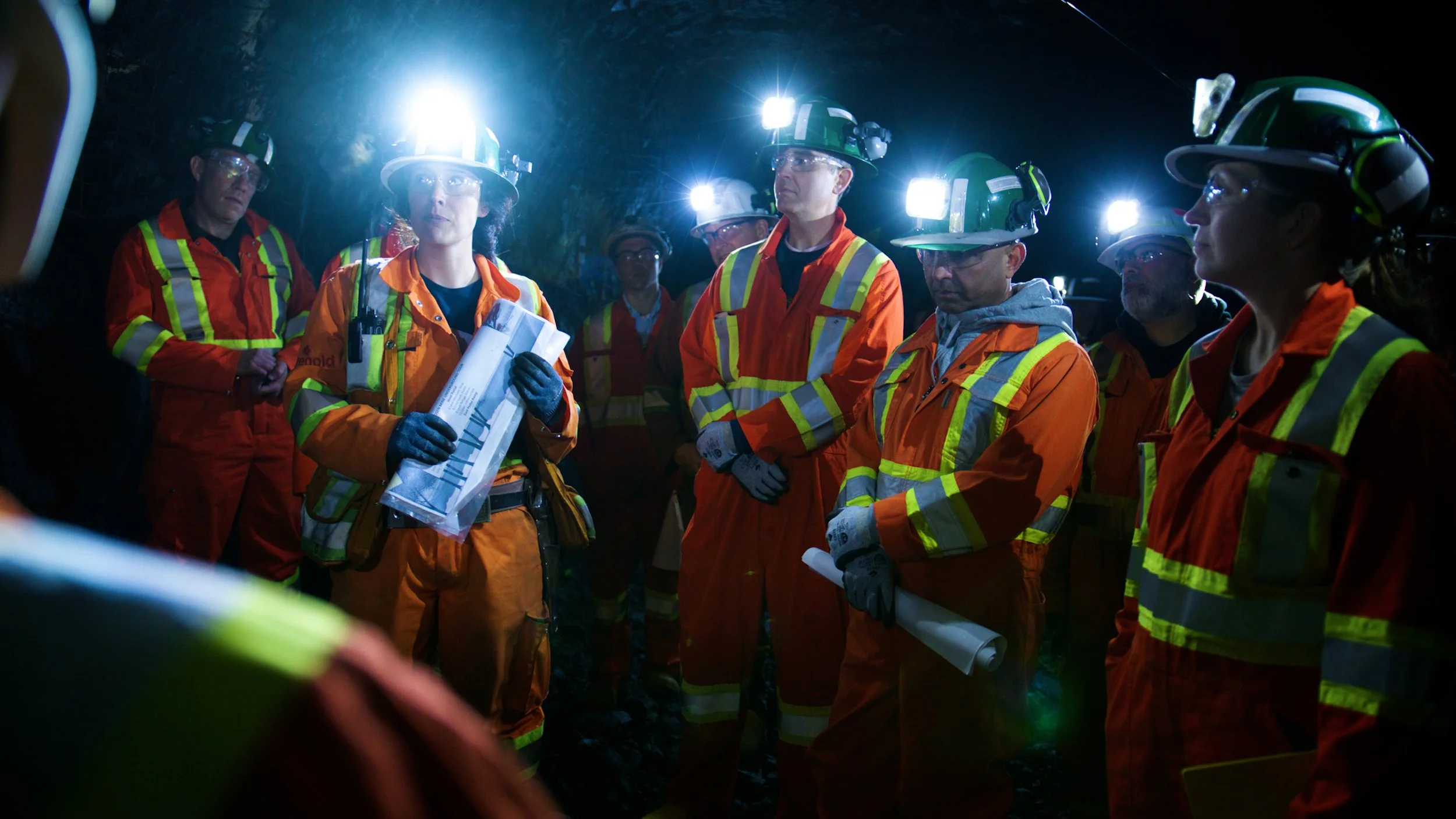 Group of investors touring an underground gold mine while reviewing site plans.
