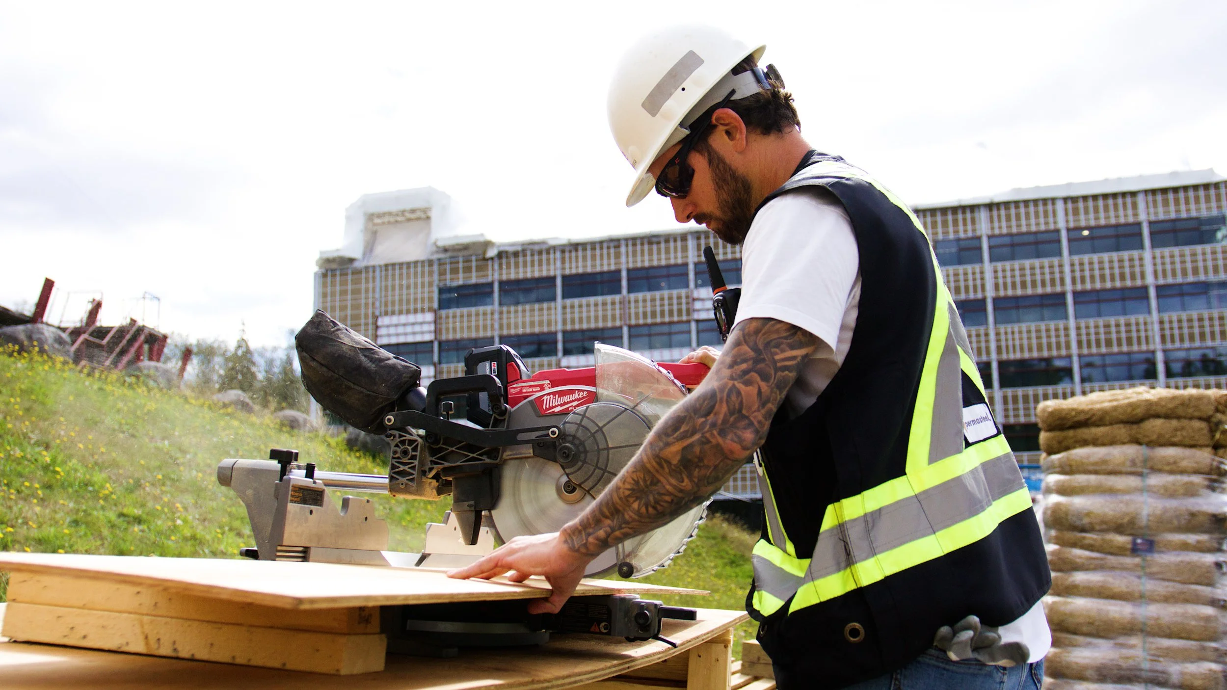 Construction worker using a miter saw to cut lumber at an outdoor job site.