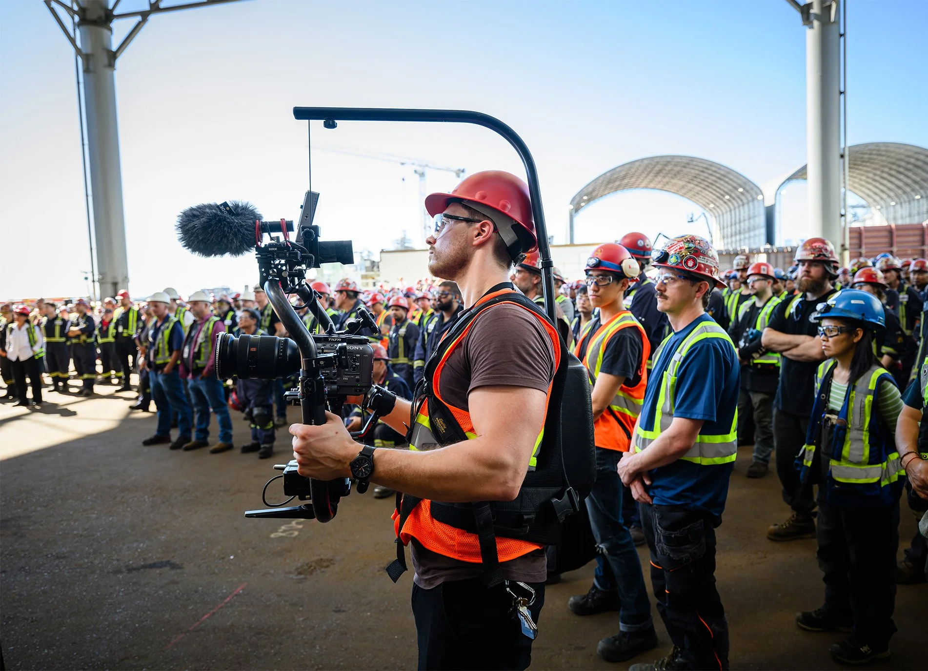 Cinematographer filming an industrial event with a cinema camera on a gimbal in a shipyard setting.