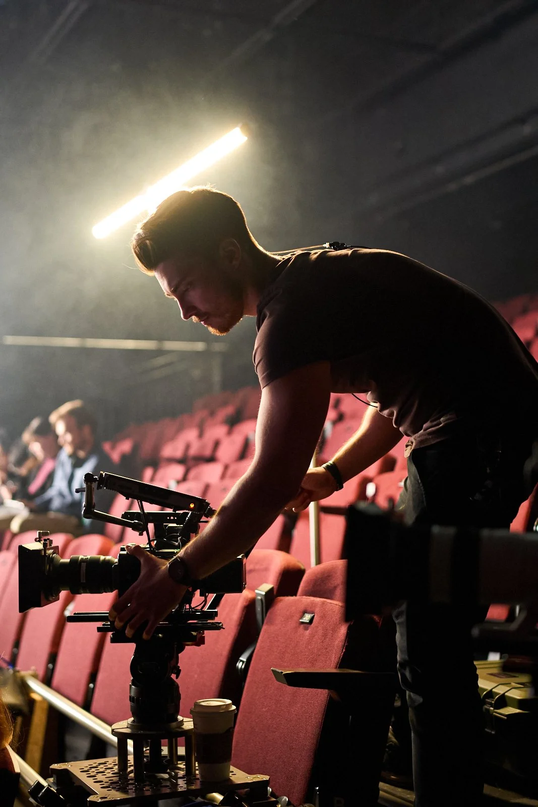 Cinematographer setting up a cinema camera in a theatre auditorium during a professional video production.