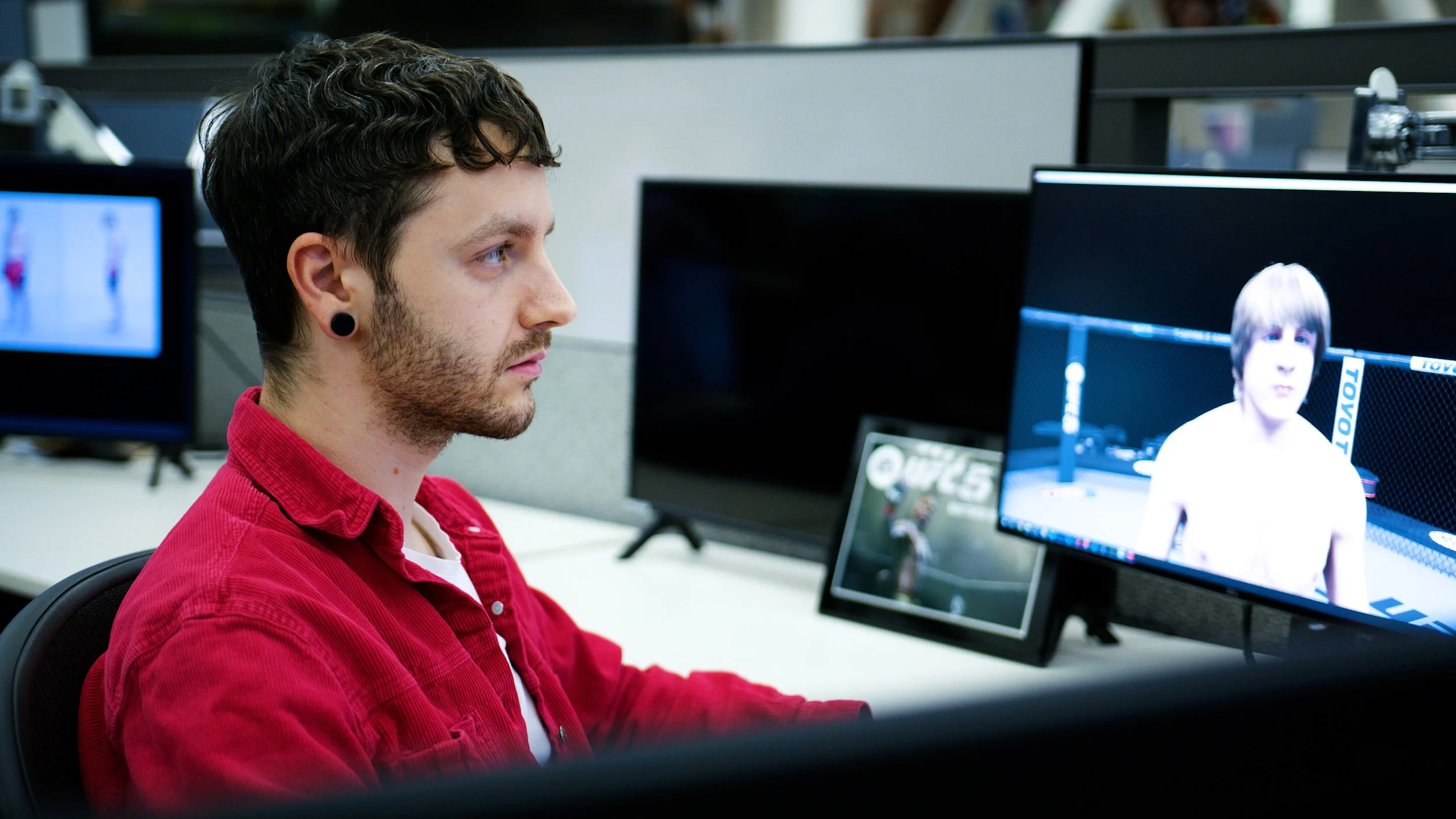 Game developer reviewing a fighter character model on a computer screen in a studio workspace.