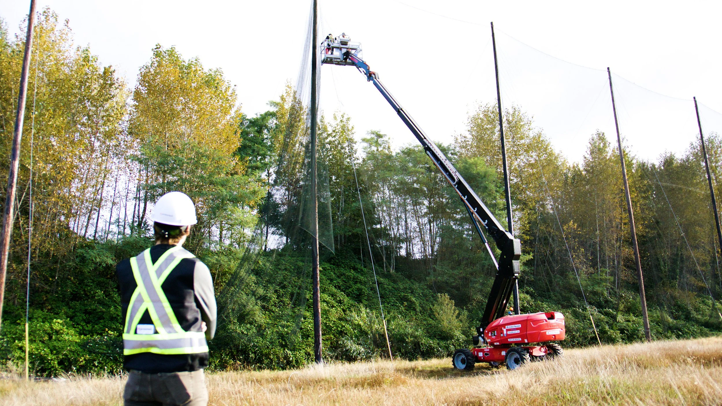 Construction worker observing a boom lift removing safety netting at a demolition site.