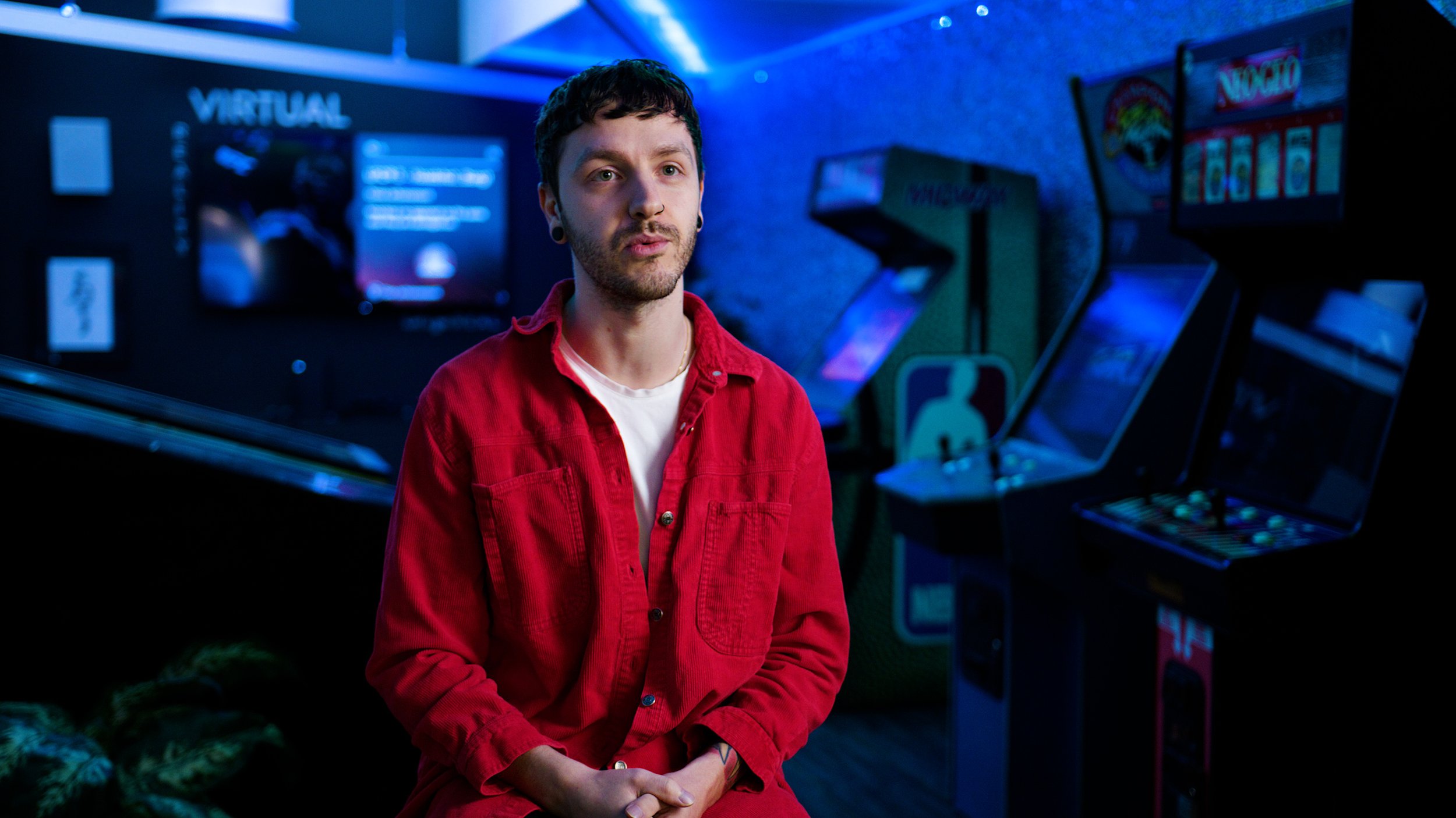 Man speaking in a neon-lit gaming studio with arcade machines in the background.