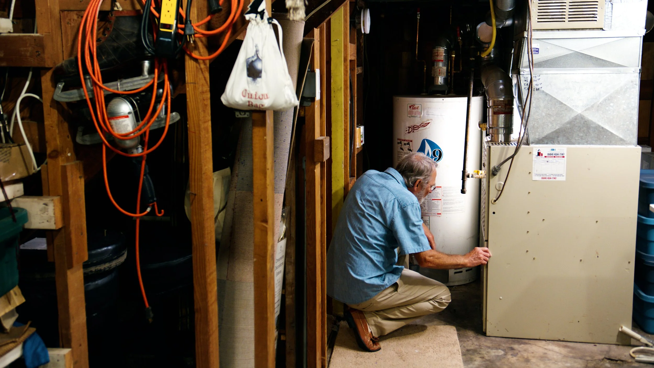 Homeowner inspecting a furnace and hot water tank in a residential basement.