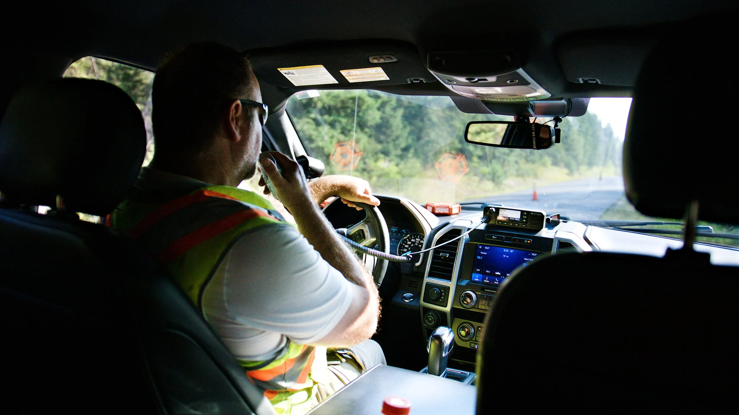 Road maintenance supervisor using a two-way radio while driving a service vehicle.