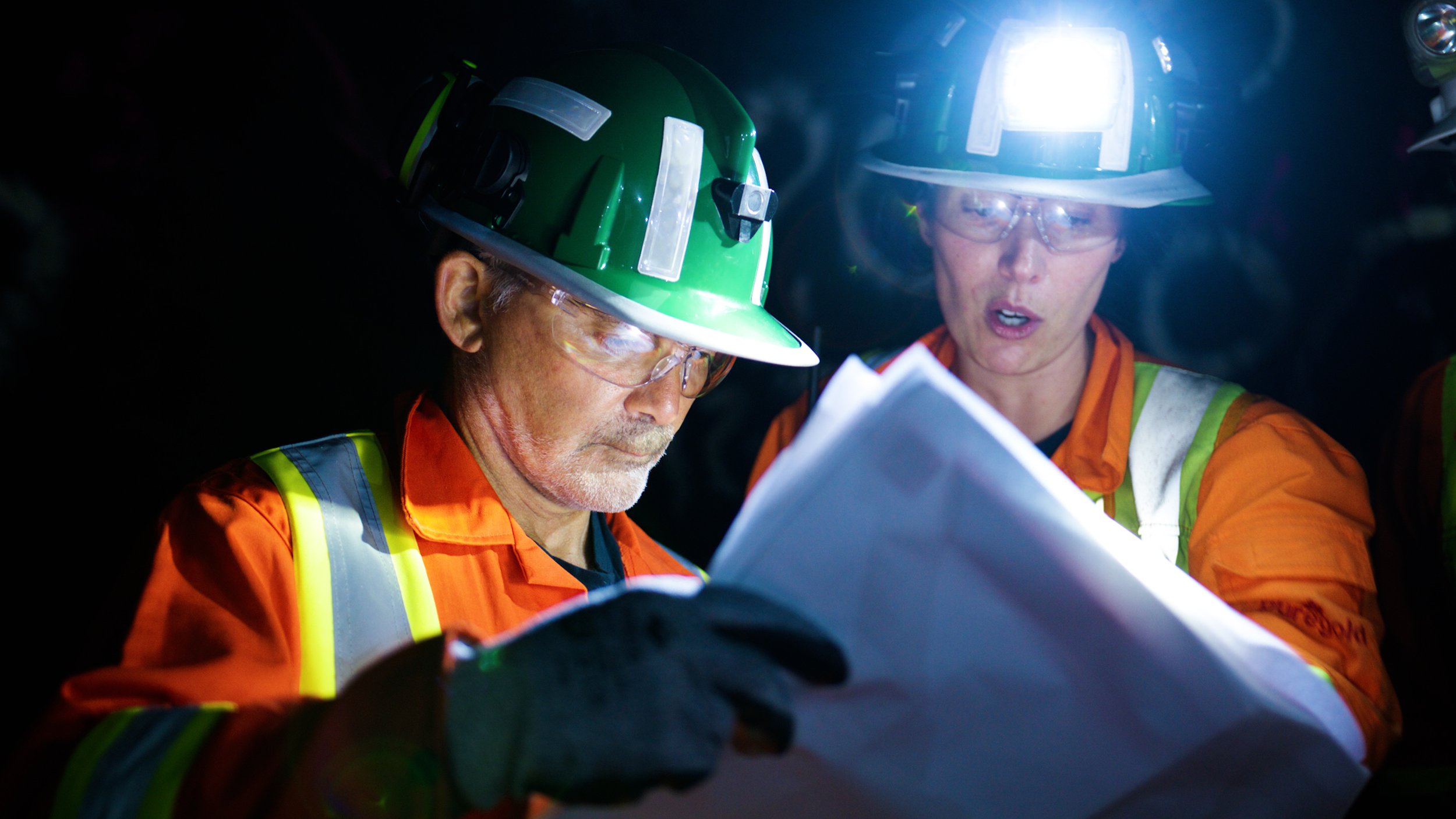 Underground mining professionals reviewing technical documents inside a gold mine.
