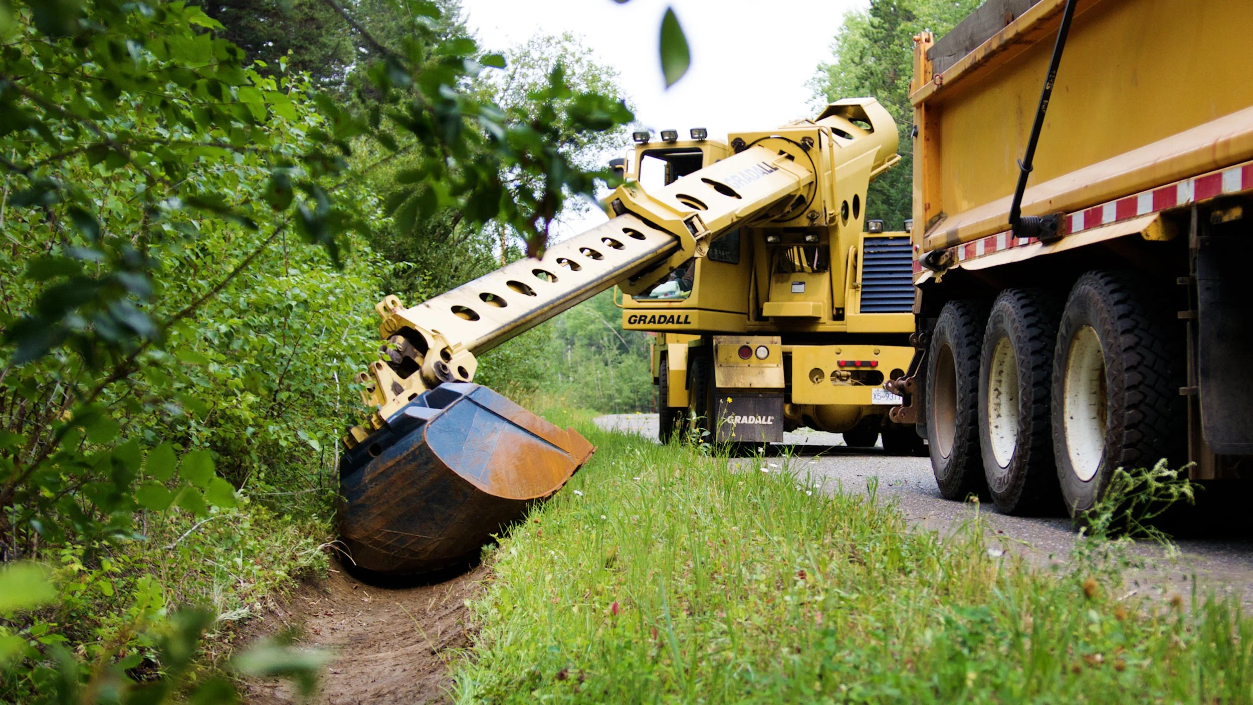 Gradall excavator cleaning a roadside drainage ditch beside a maintenance truck.