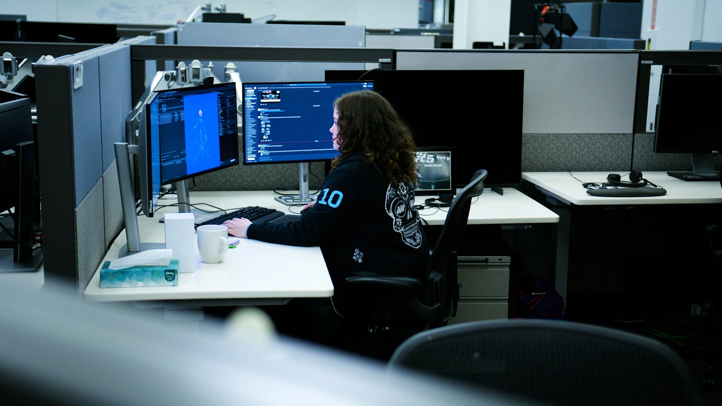 Game developer working at a computer displaying a 3D character rig in a studio workspace.