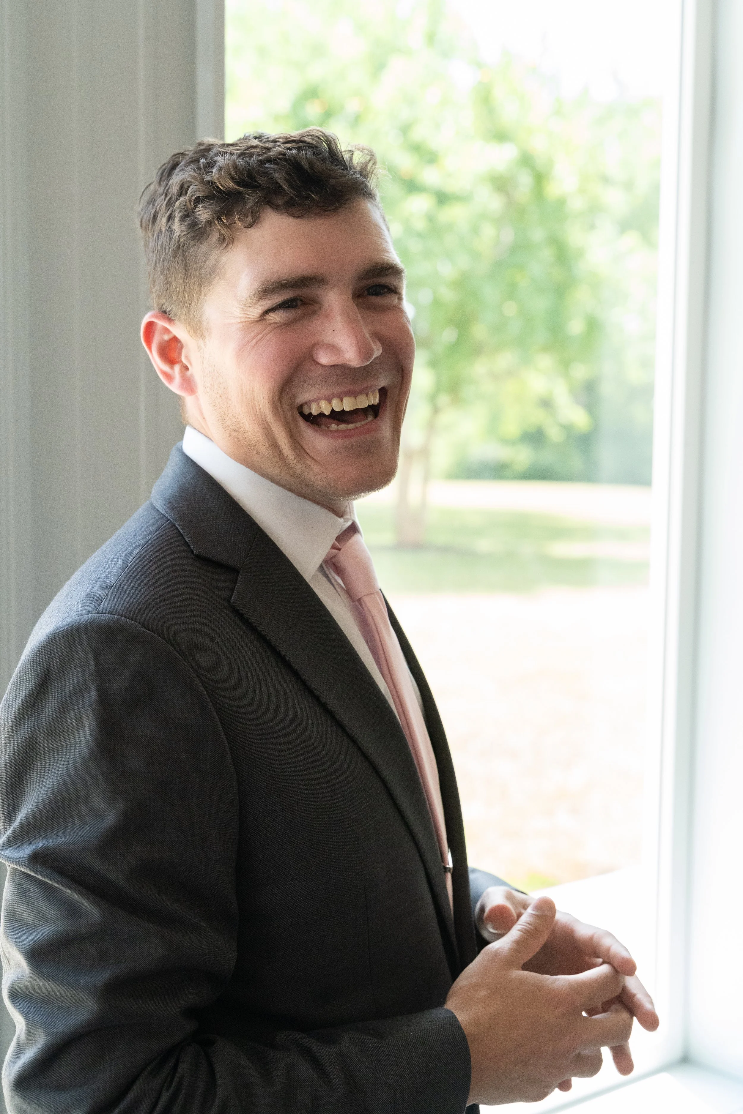 This is a scenic boho rustic view of the groom inside of The Magnolia Barn award-winning reception hall outdoor barn wedding venue featuring an exposed brick wall with natural light in Miamisburg at Magnolia Estate. Surrounded by the Greater Dayton, 