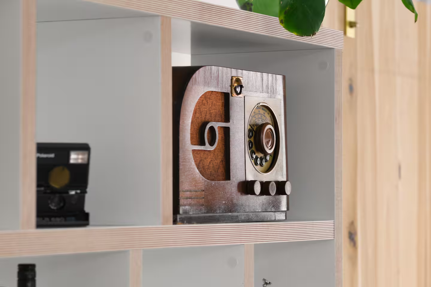 Vintage wooden radio with round dial and three knobs, placed on a light-colored wooden shelf.