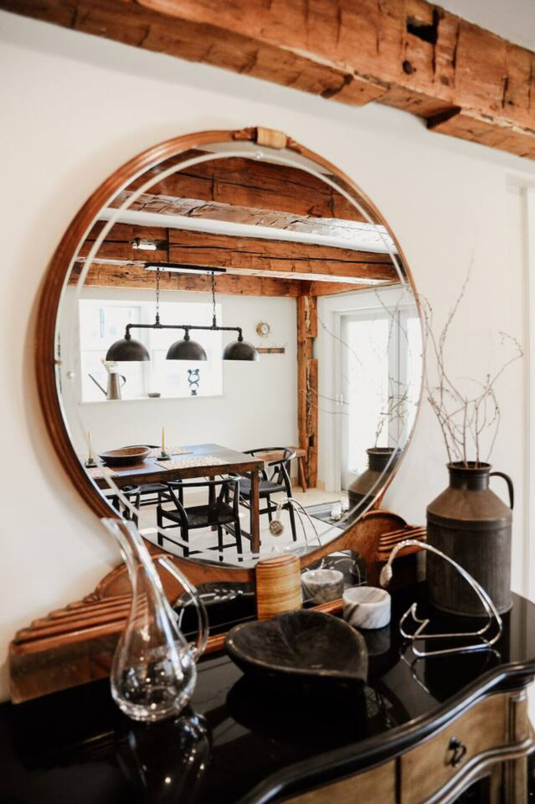 A round mirror reflecting a dining room with wooden beams, a table with black chairs, and three black pendant lights.
