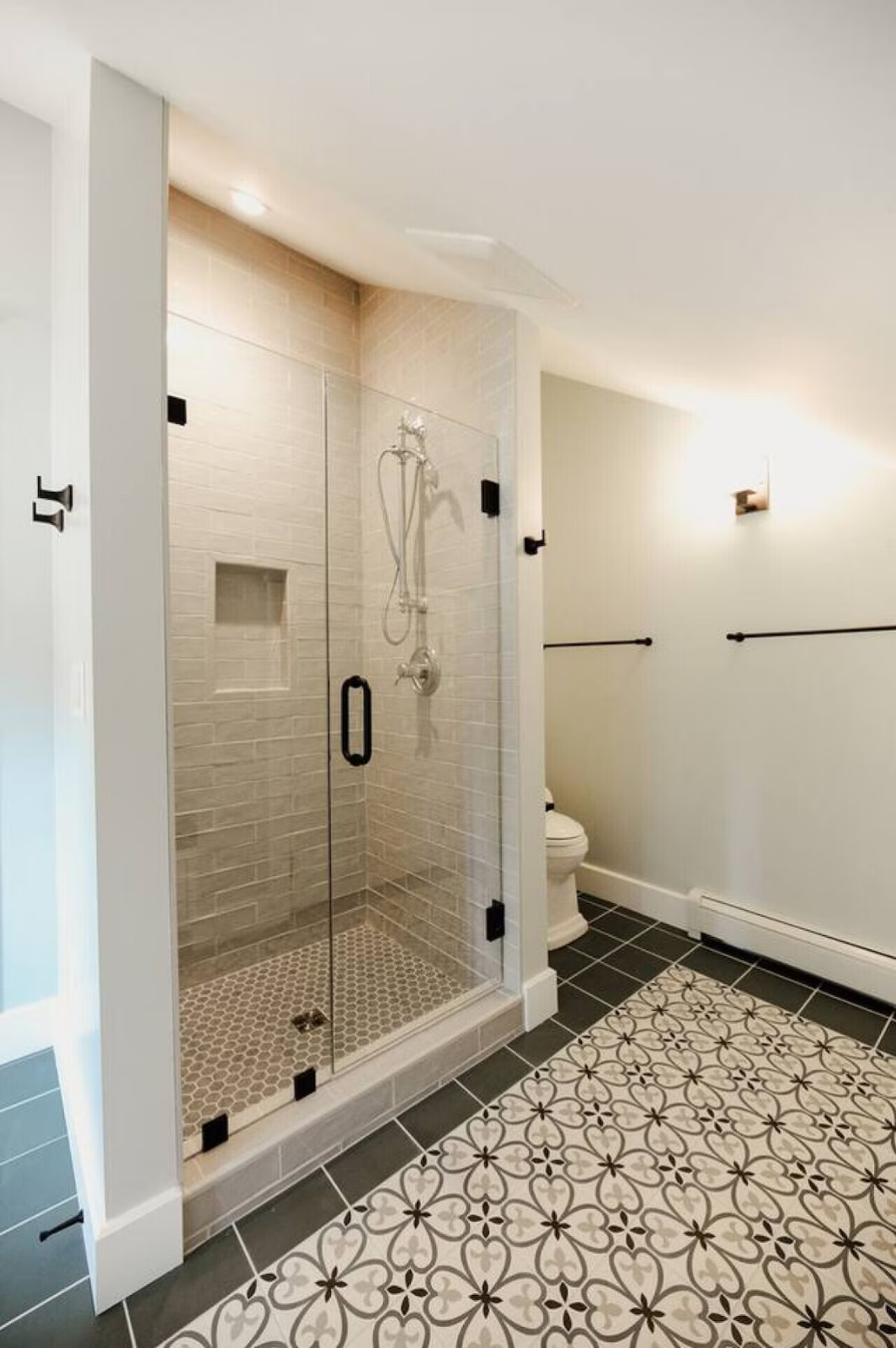 A modern bathroom with a glass-enclosed shower, tiled shower walls, a toilet, and patterned floor tiles.