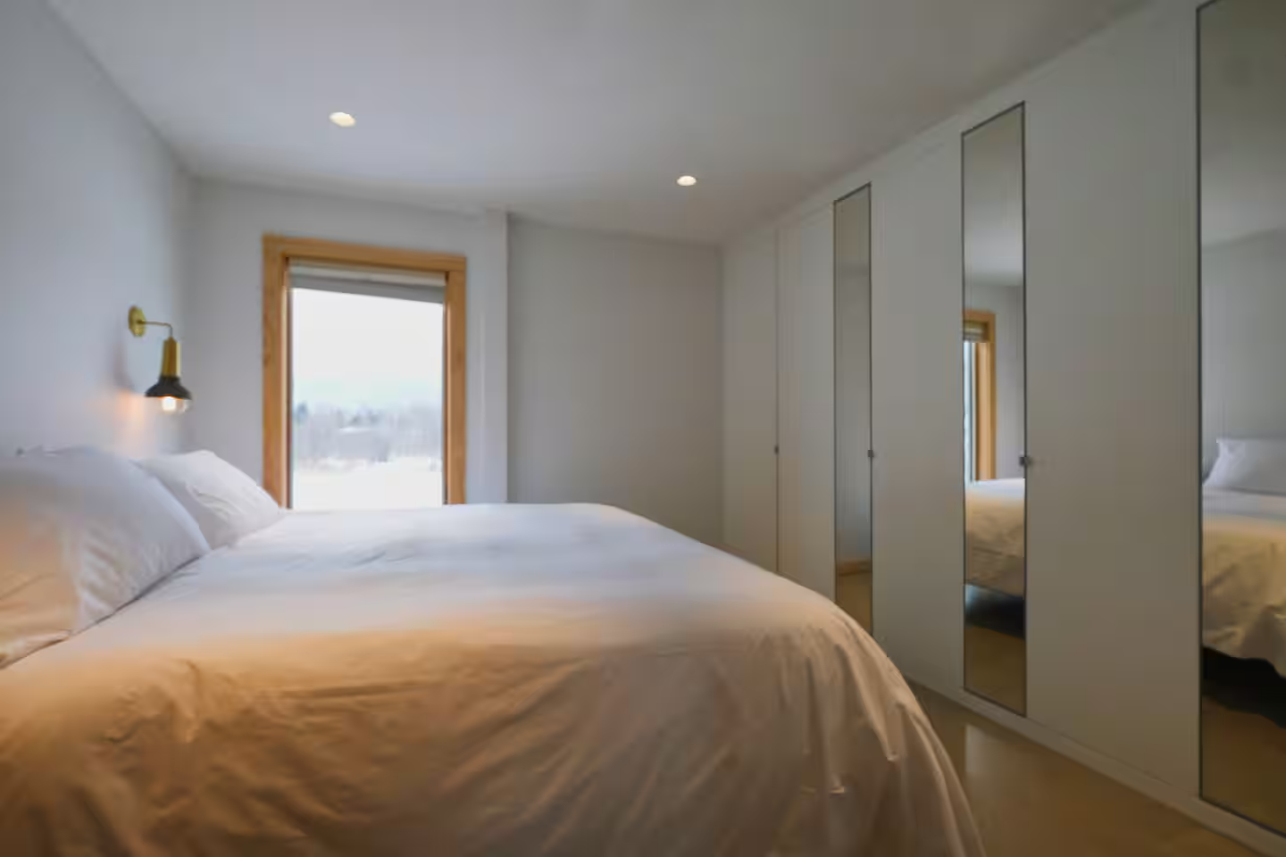 Bedroom with white bedding, wooden window frame, and mirrored closet doors.