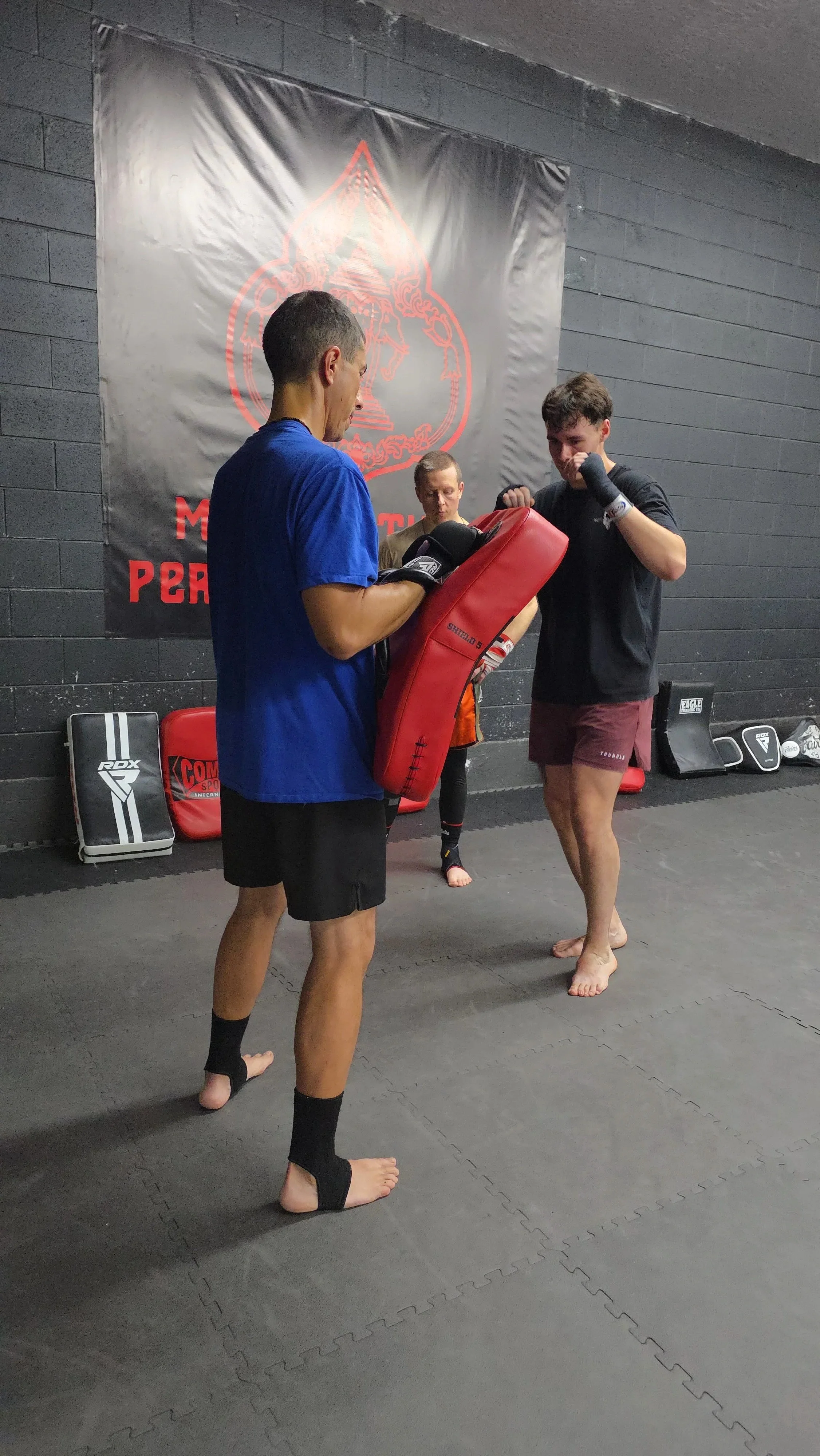 A group of martial arts students practicing agility ladder drills in a black-walled training center with Thai and MMA training branding.