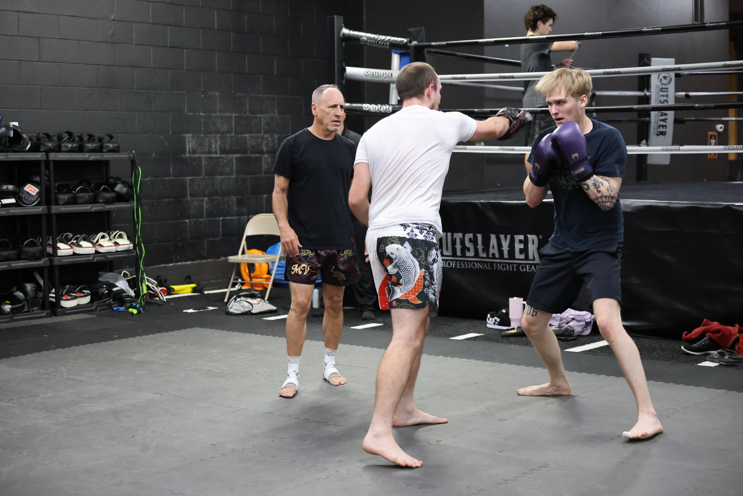A group of martial arts students practicing agility ladder drills in a black-walled training center with Thai and MMA training branding.
