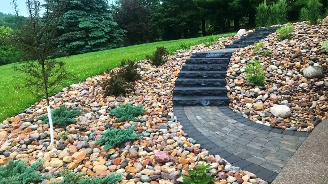 Landscape with stone steps, a curved brick pathway, and landscaped garden with small plants, rocks, and trees.