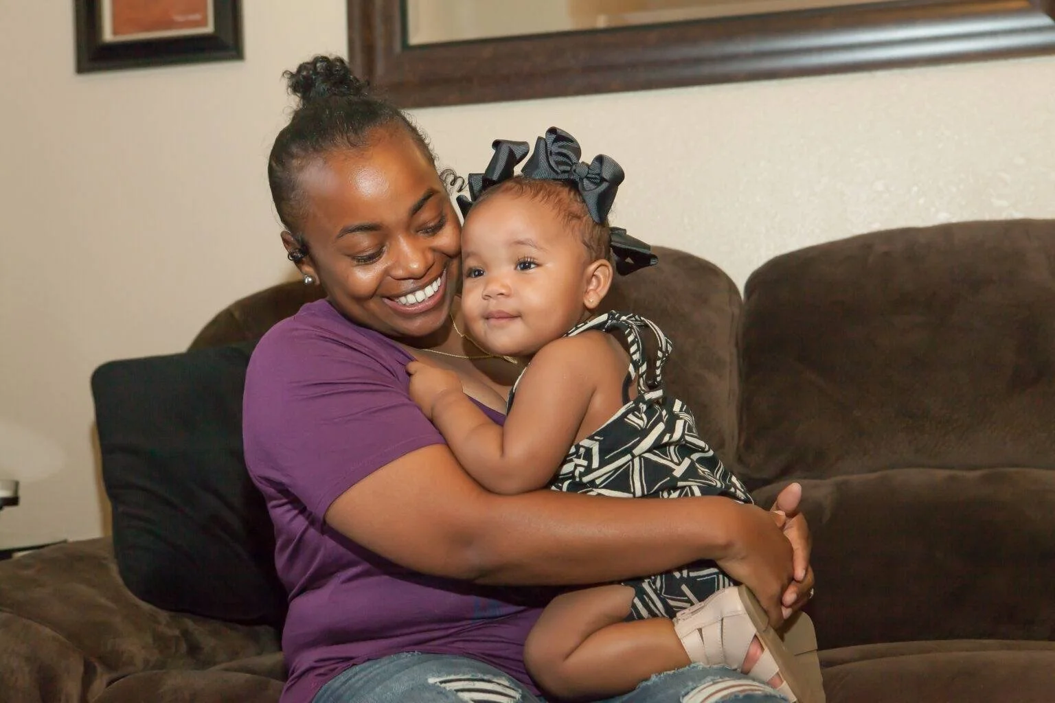 Smiling caregiver seated on couch embracing child held on lap.