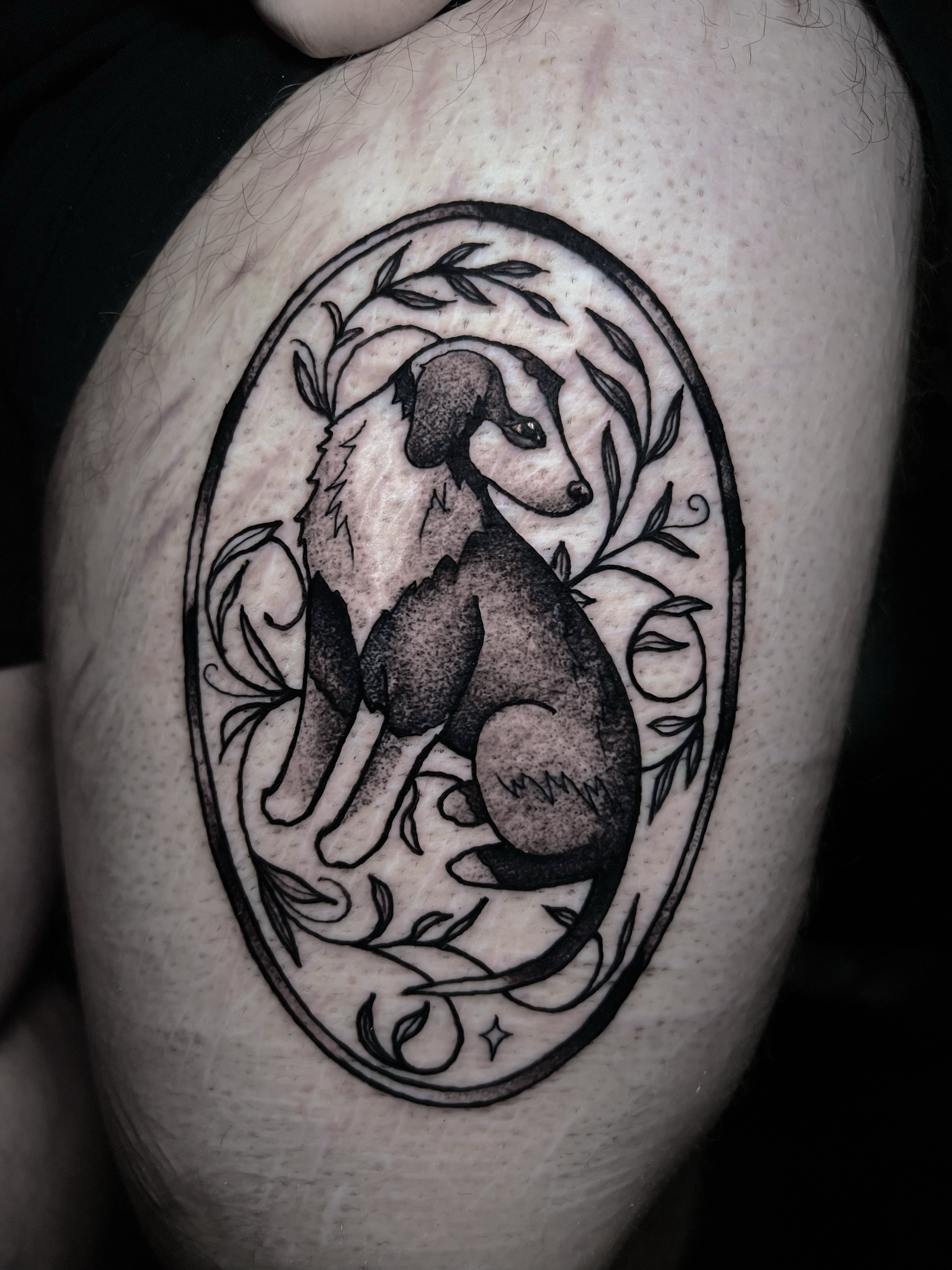 A tattoo of a stylized fox's head inside an oval frame, surrounded by leaves and small decorative elements, on a person's skin.