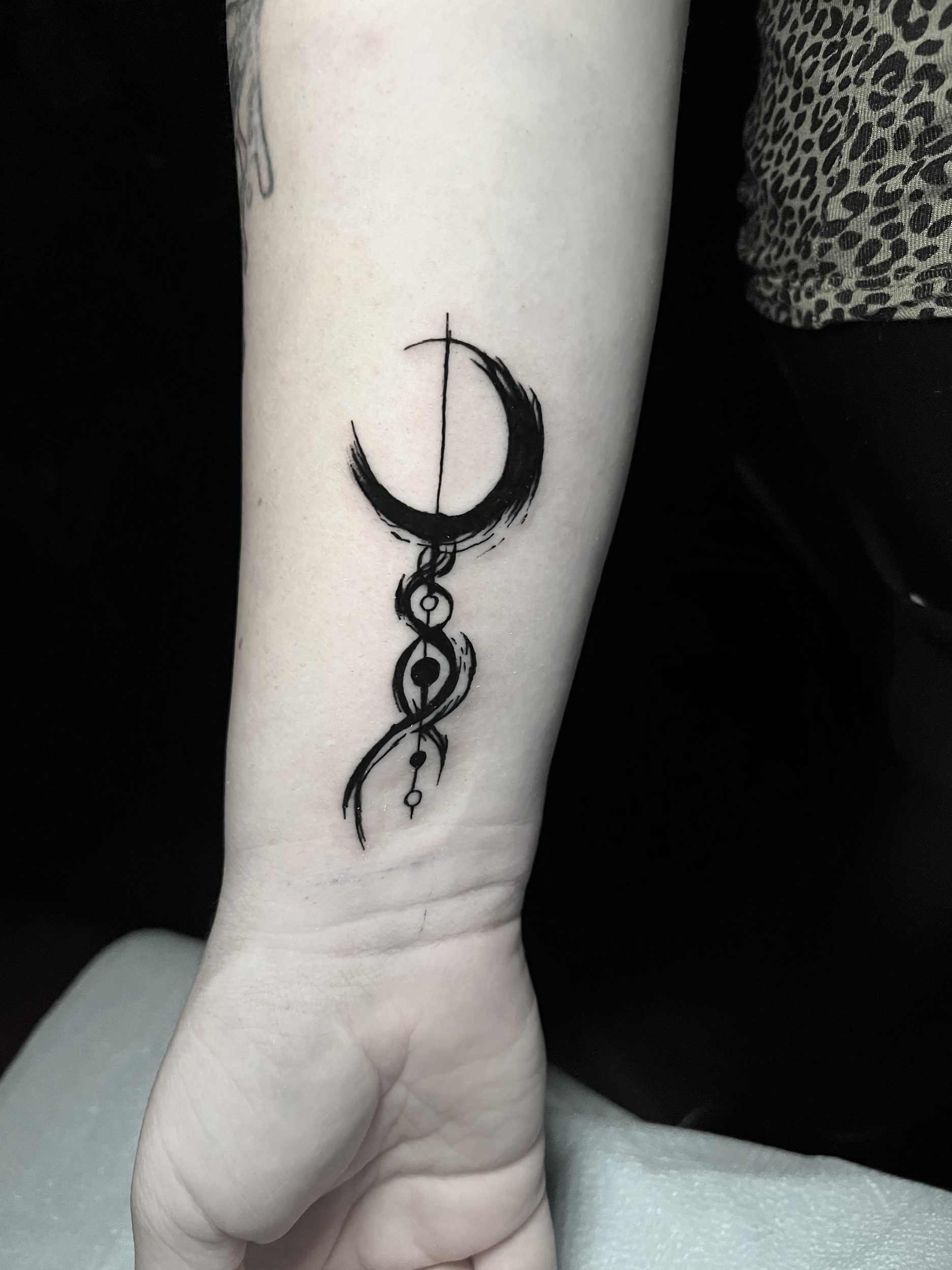Tattoo of a crescent moon and celestial symbols in black ink on inner forearm.